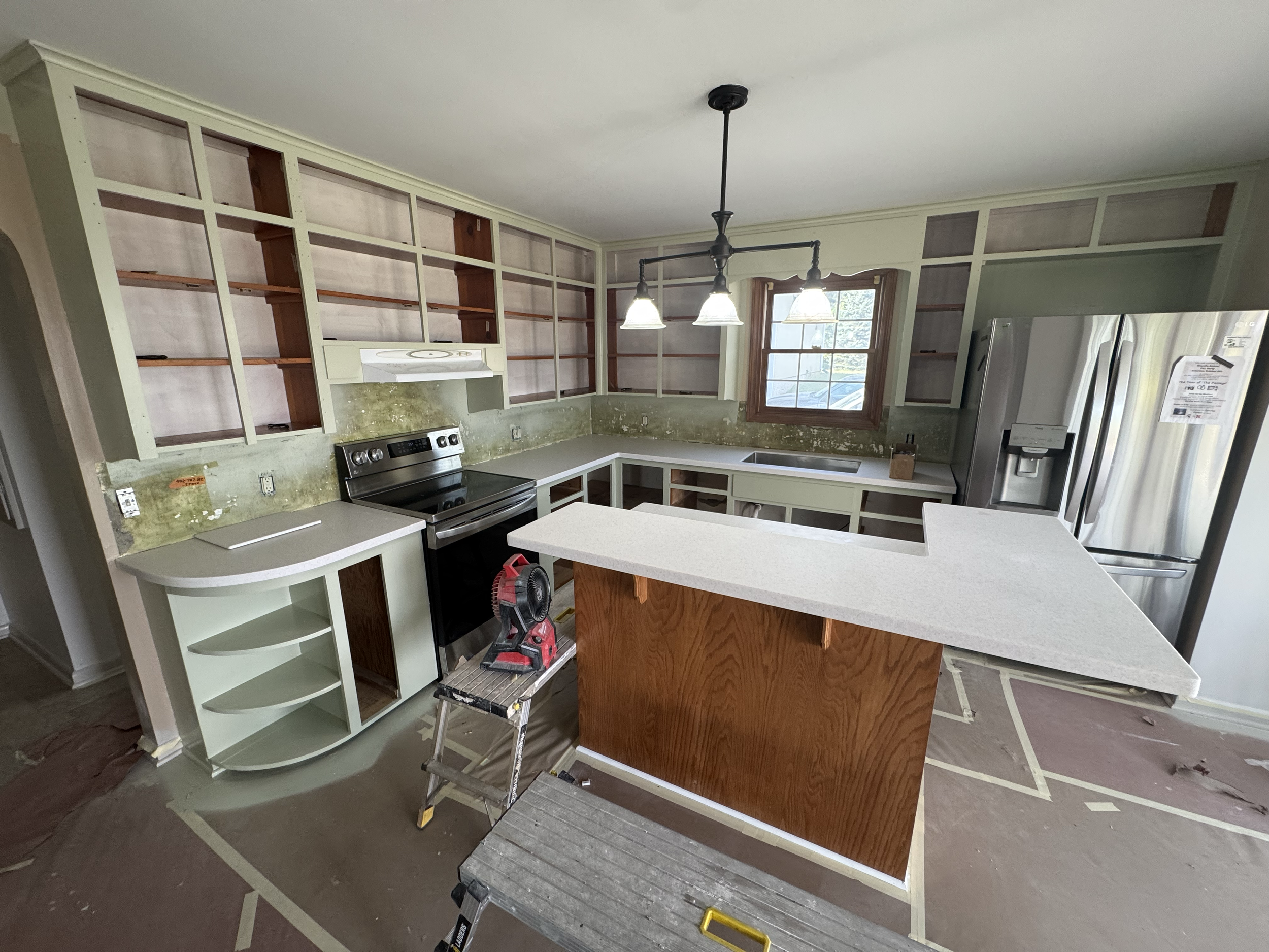 Kitchen under renovation with open cabinets, a stainless steel refrigerator, and construction tools.