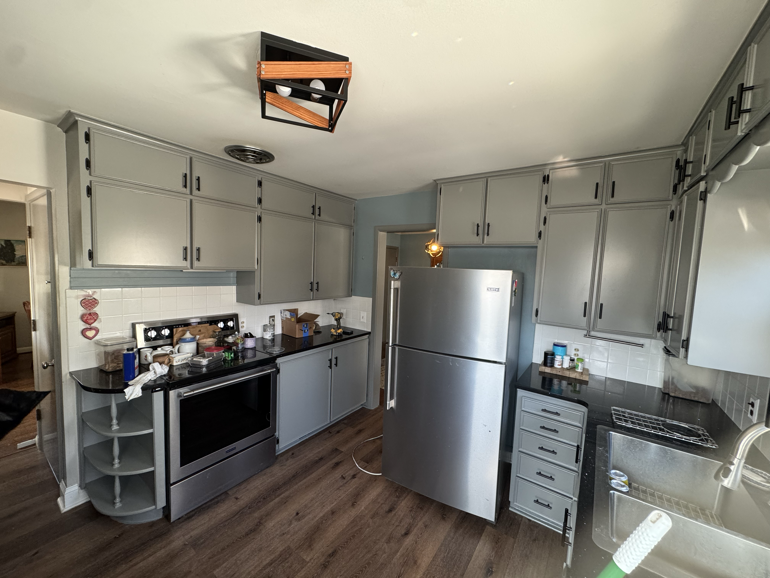 Kitchen with white cabinets, black countertops, and stainless steel appliances. A messy stove and various items on the counter, including boxes and tools.
