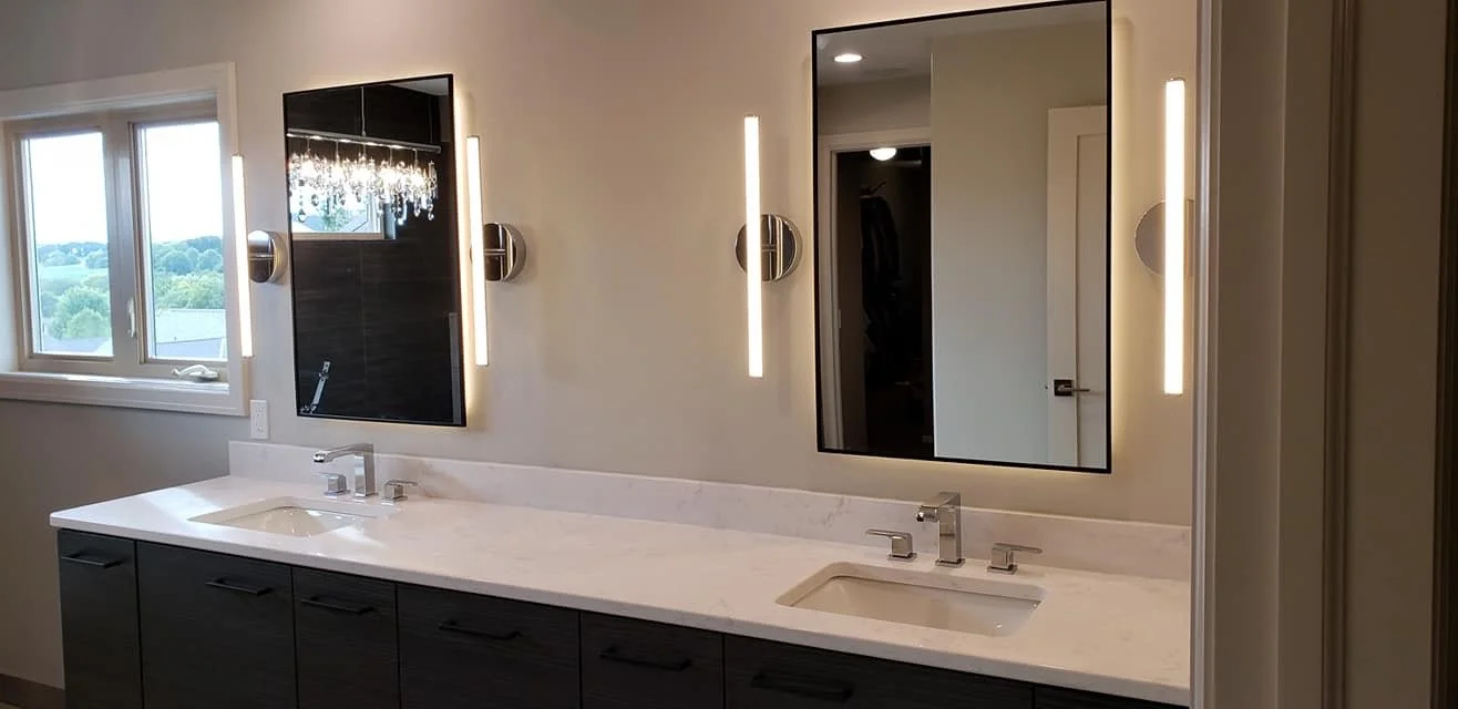 Bathroom vanity area with dual sinks, modern black cabinets, white marble countertops, and two large framed mirrors with vertical LED lights on each side, near a window with a scenic view.