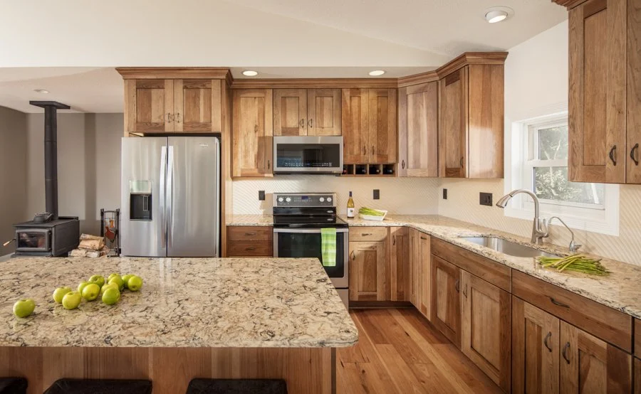 Kitchen with wooden cabinets, granite countertops, stainless steel appliances, a stove, built-in microwave, refrigerator, and a window above the sink. Green apples and celery on the counters.