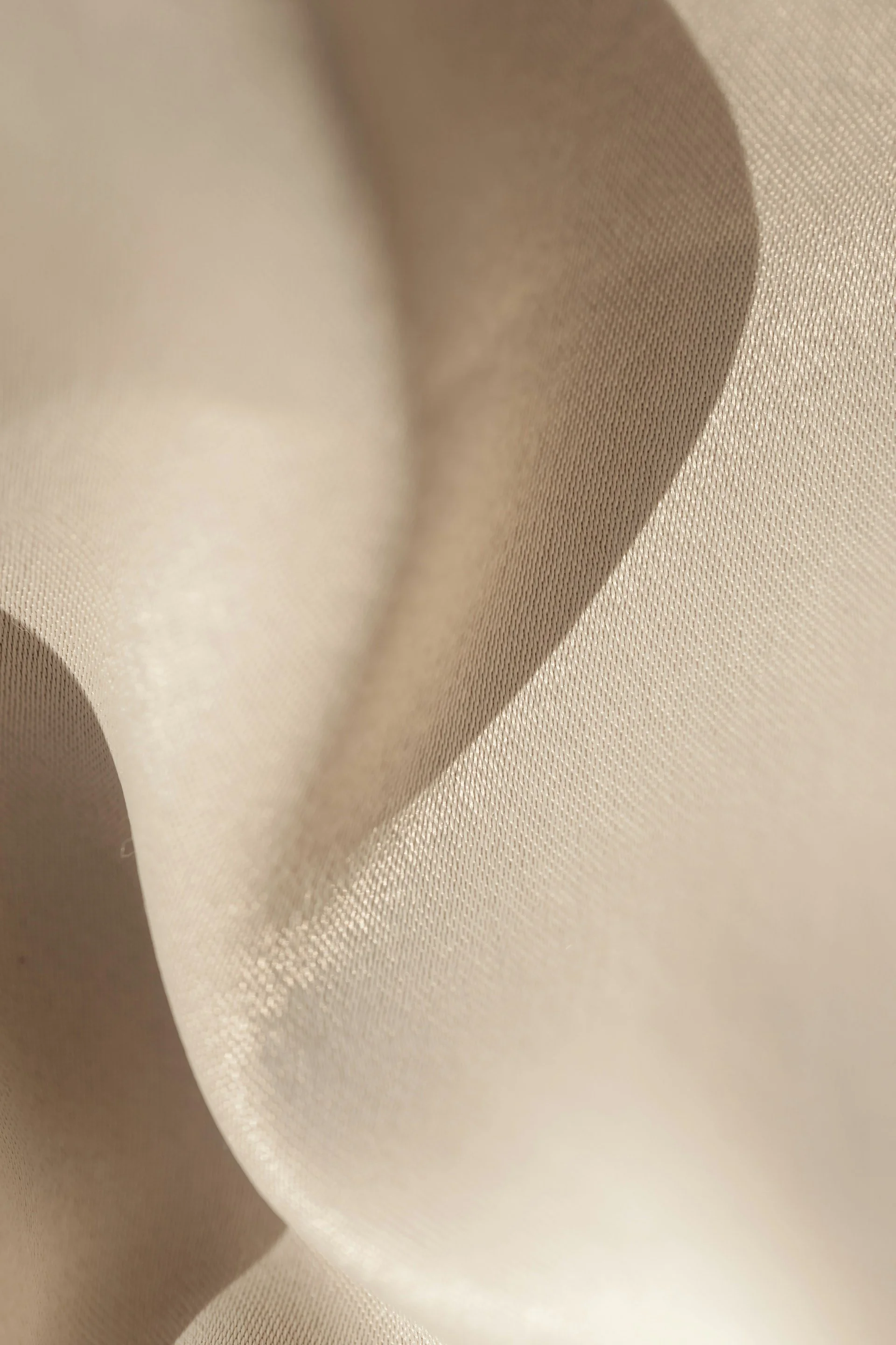 Close-up of beige fabric with a smooth texture and subtle sheen, showing folds and gentle curves.