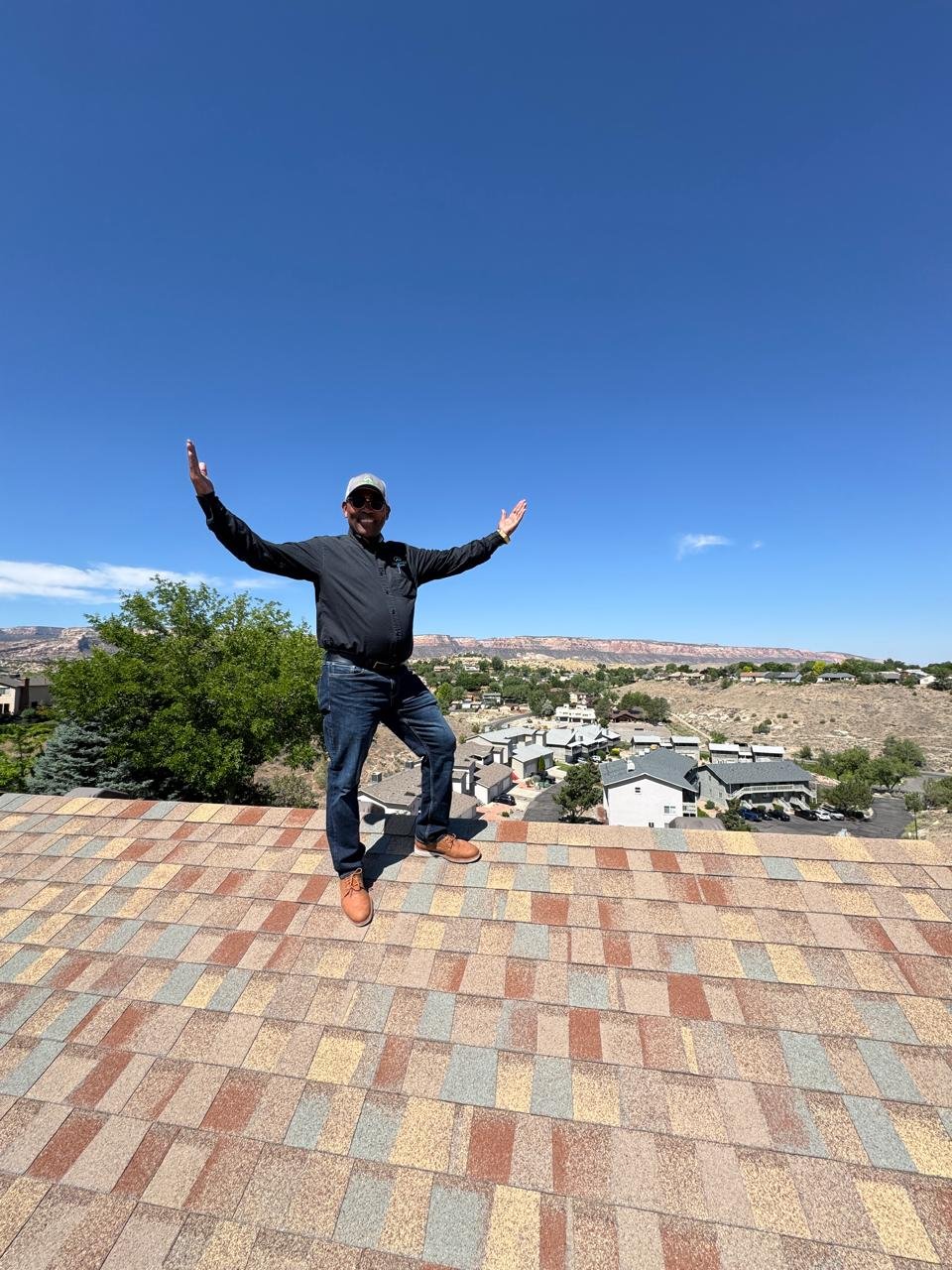 Man standing on the rooftop with arms wide open, smiling, cityscape and mountains in the background under a clear blue sky.