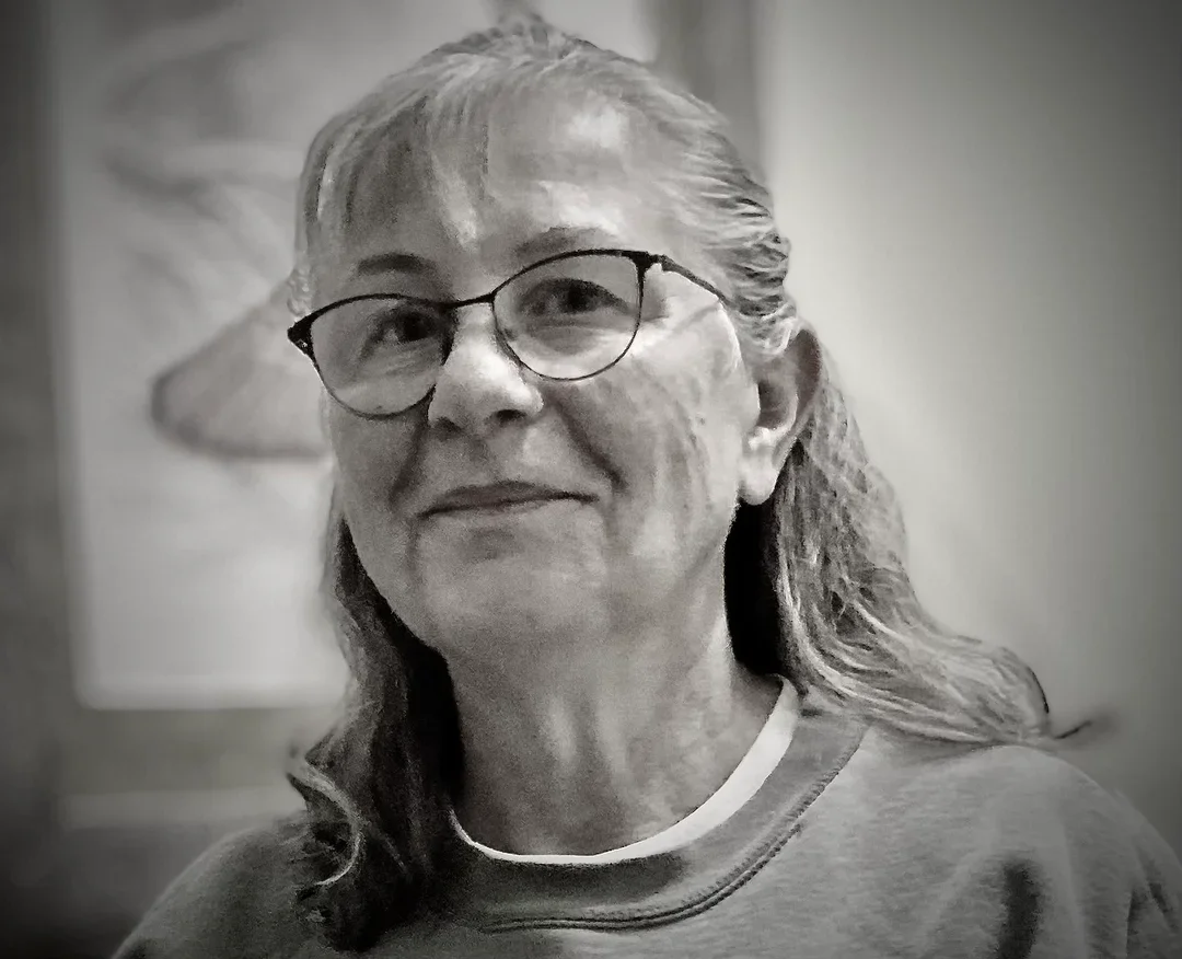 Black and white photo of an elderly woman with glasses, smiling gently, wearing a sweatshirt.