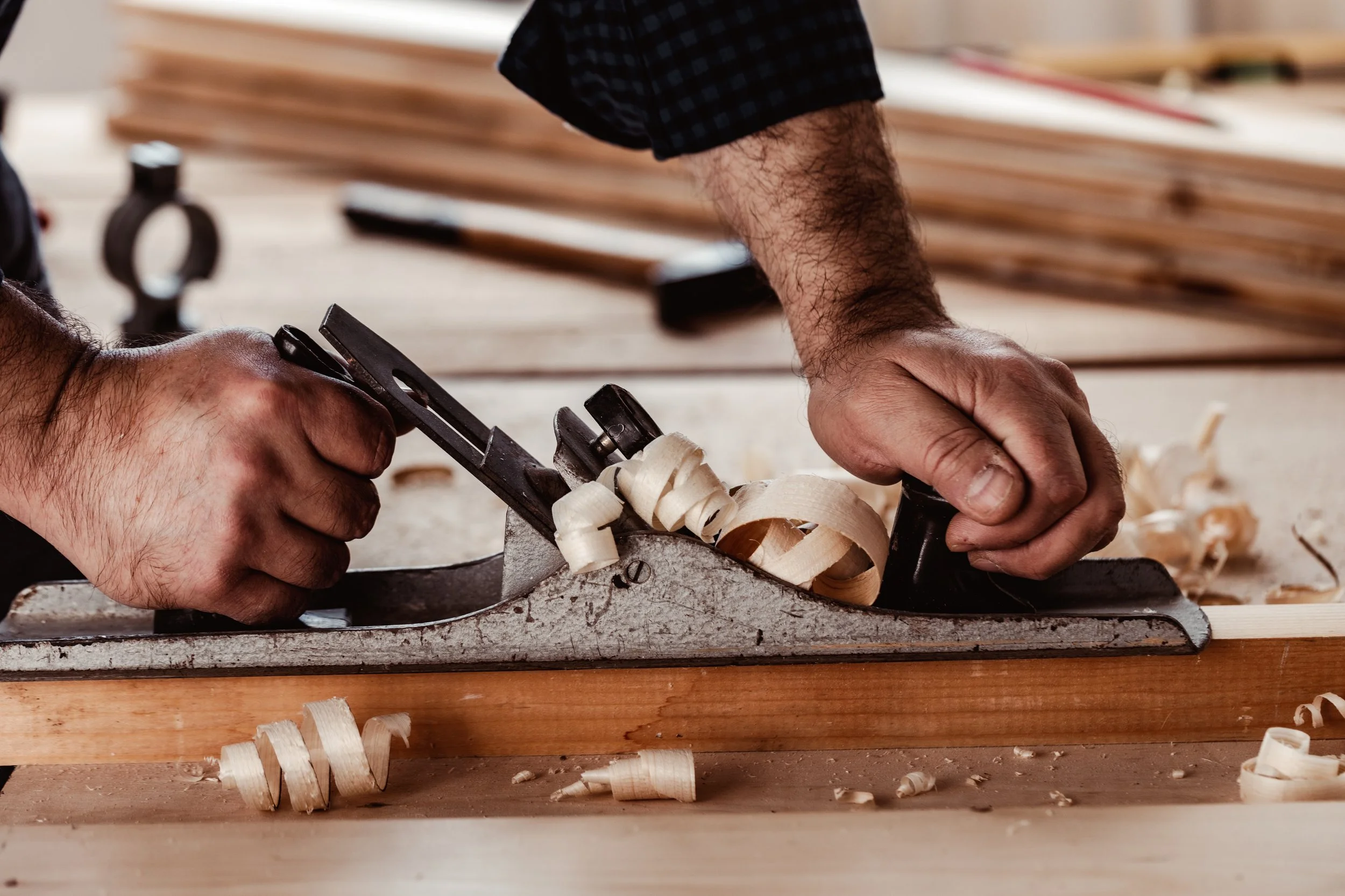 Person using a hand plane to smooth wood shavings in a woodworking shop.
