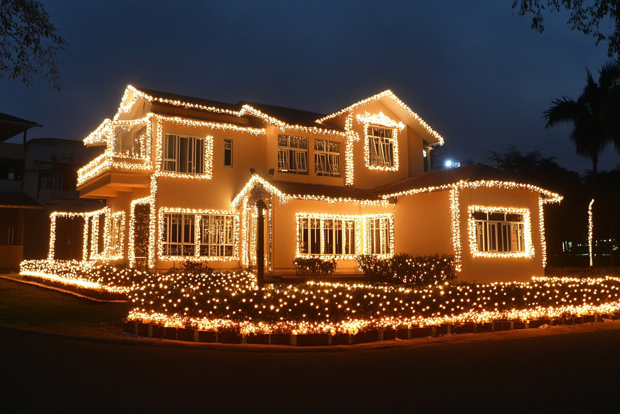 A two-story house decorated with string lights outlining the roof, windows, and entrance for a holiday or festive occasion at night.