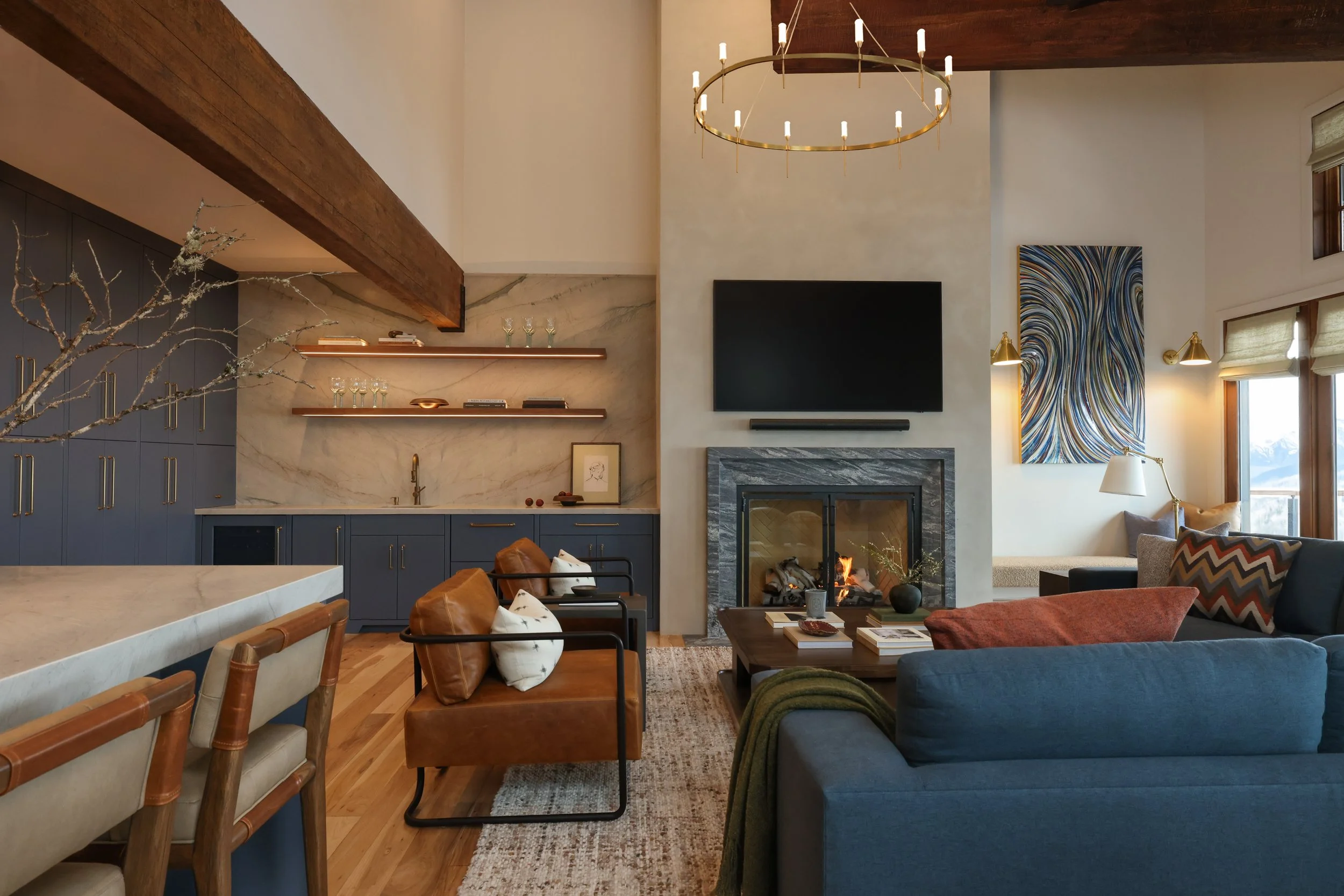 Living room with a stone fireplace, wall-mounted TV, abstract wall art, and a chandelier in a modern home.