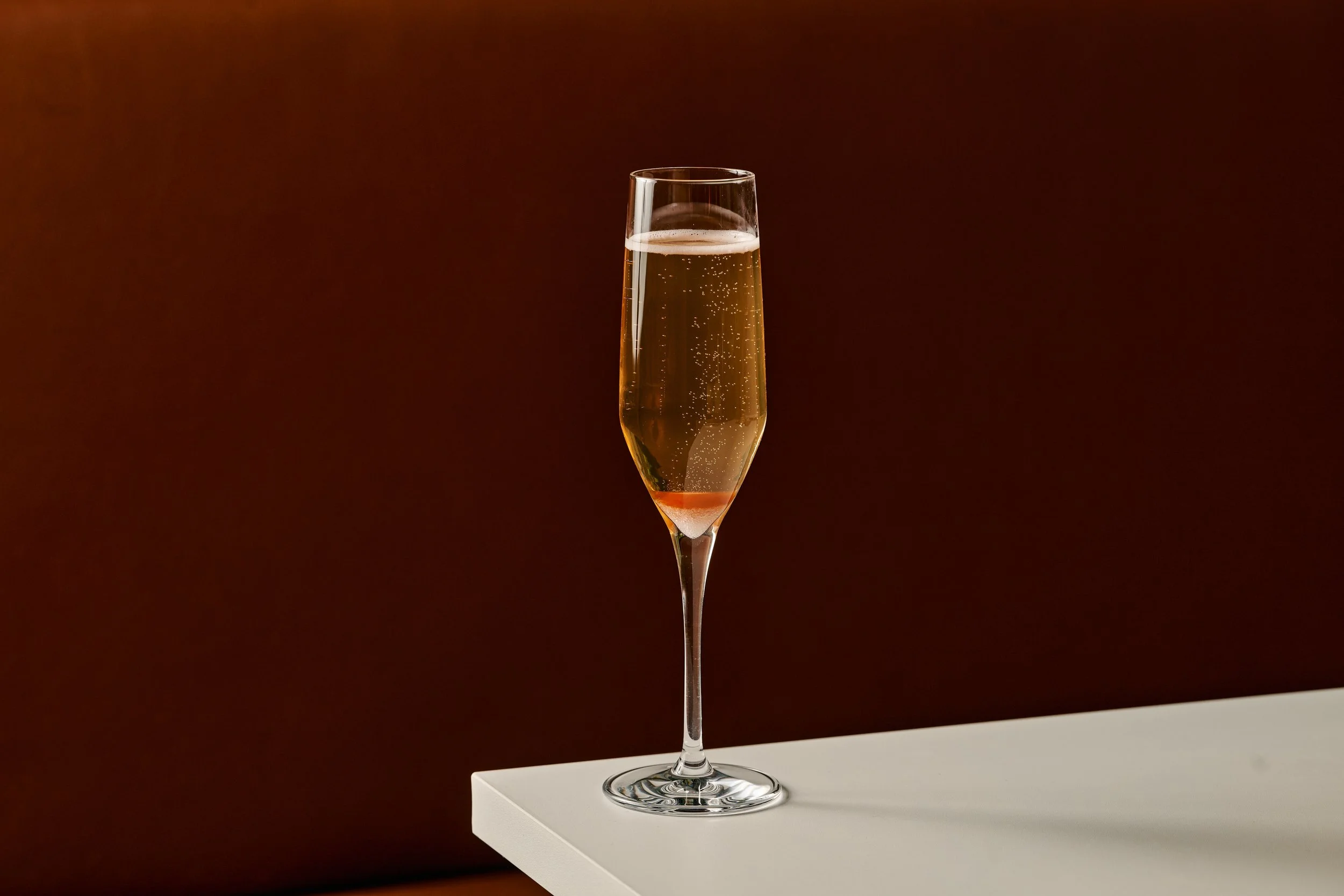 A glass of champagne on a white stand with a dark background.