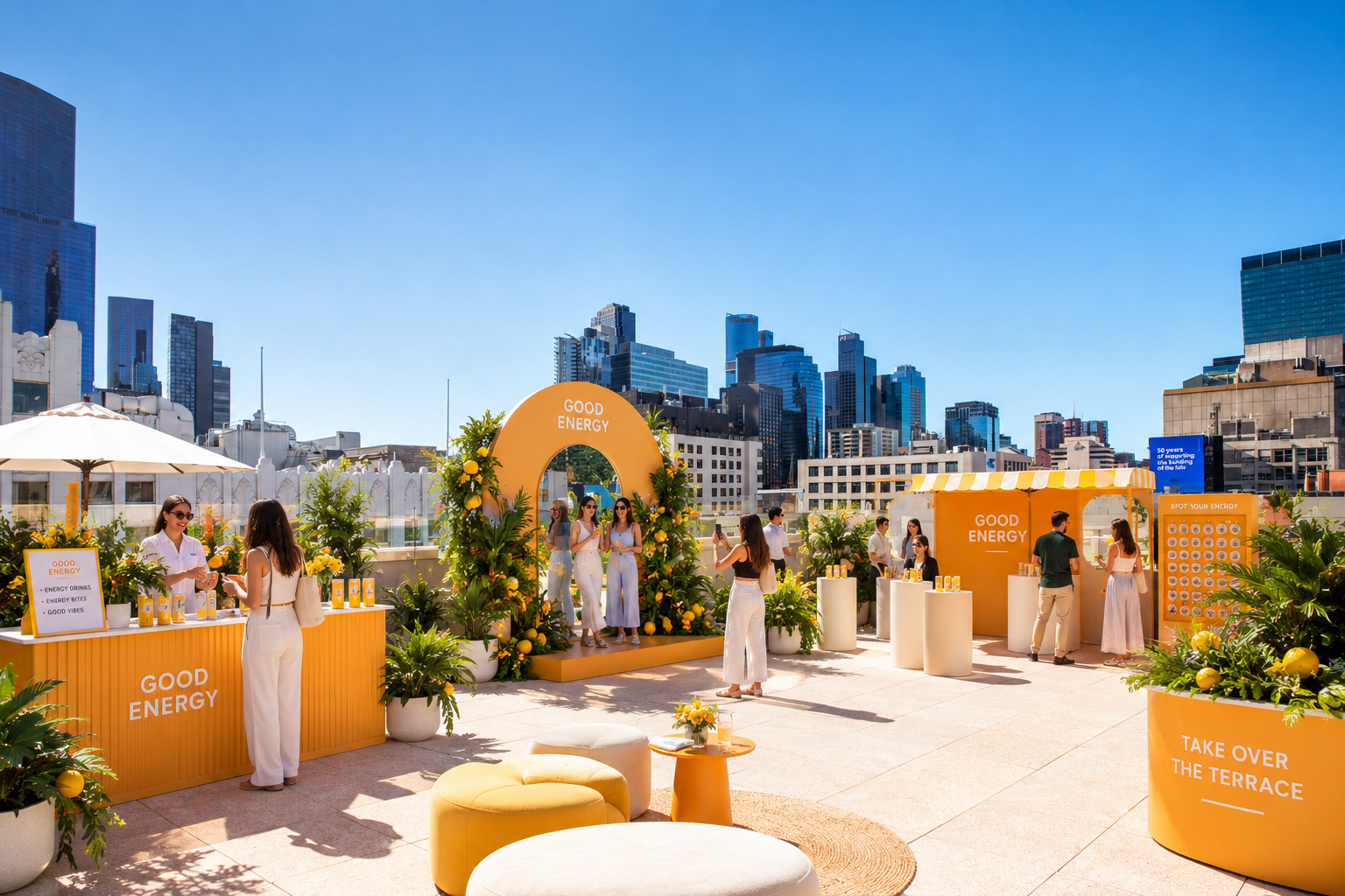 Outdoor event with yellow and white decor, plants, and city skyline in the background. People are gathered around booths labeled 'Good Energy' and 'Take Over the Terrace,' engaging with displays and taking photos under a sunny sky.
