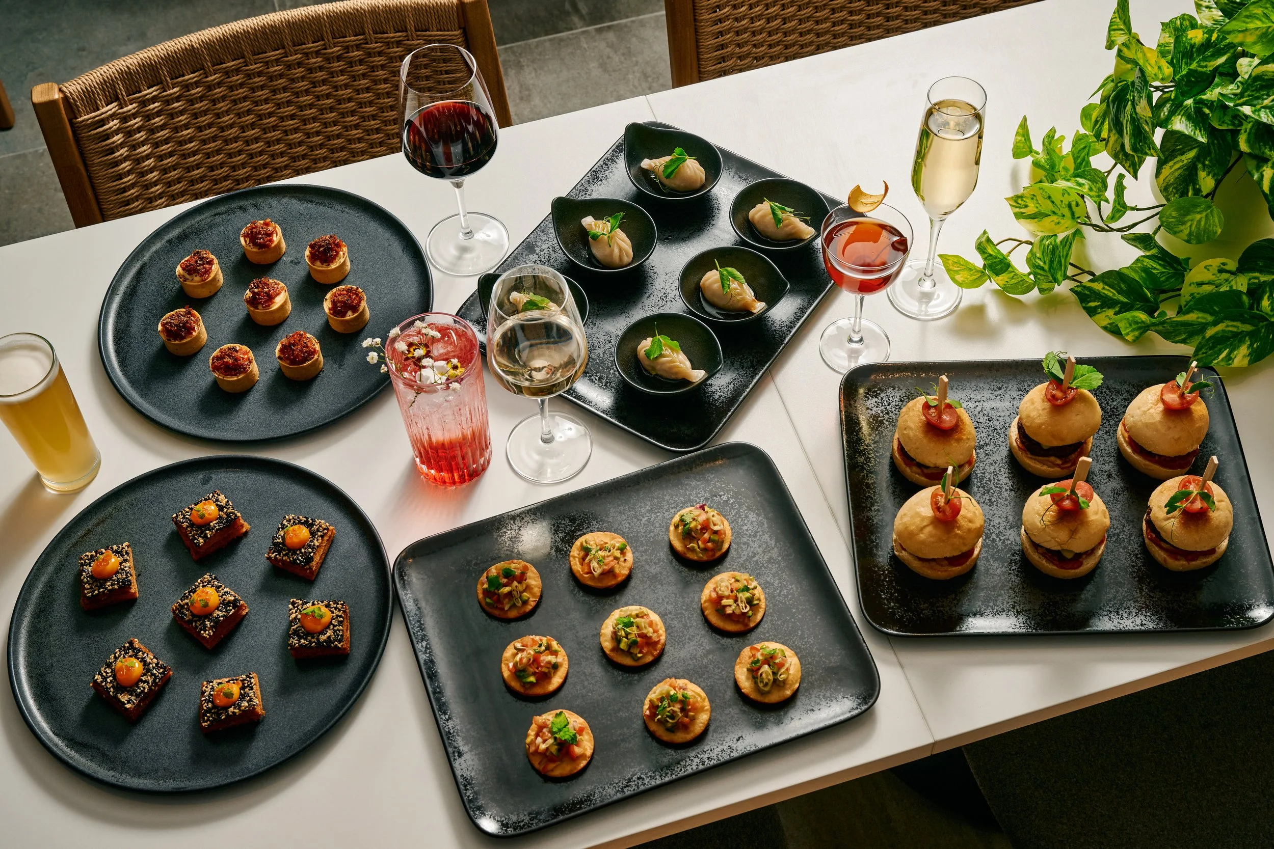 Assorted appetizers and drinks on a dining table, including small bites, glasses of wine and champagne, and a potted plant.