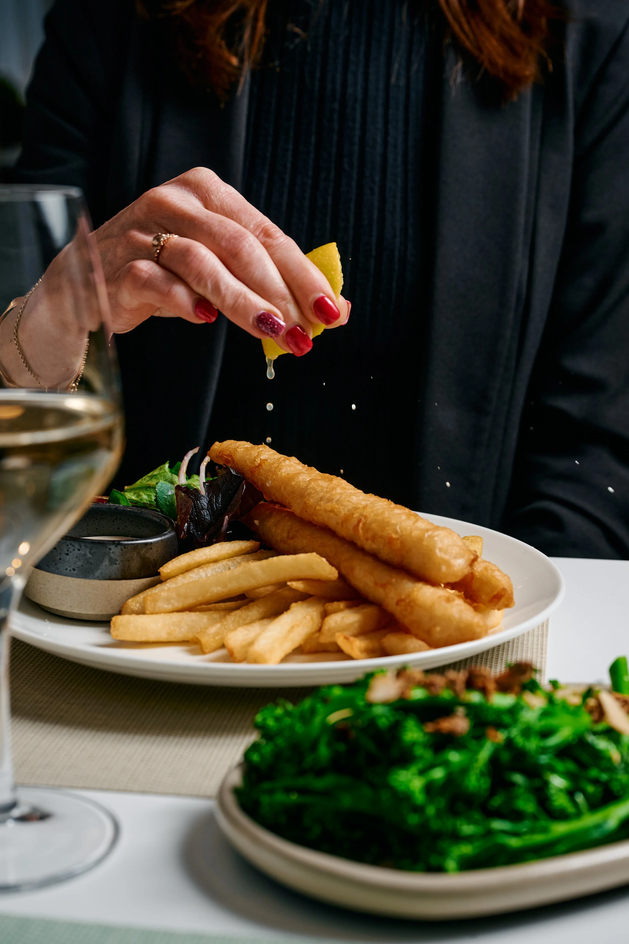 Person squeezing lemon over a plate of French fries and salad in a restaurant setting.
