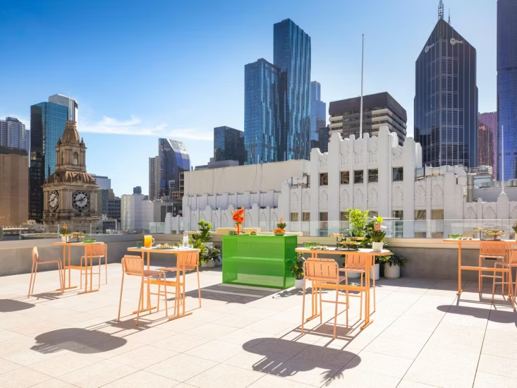 Rooftop patio with tables and chairs, city skyline with tall modern skyscrapers and historic buildings in the background during daytime.