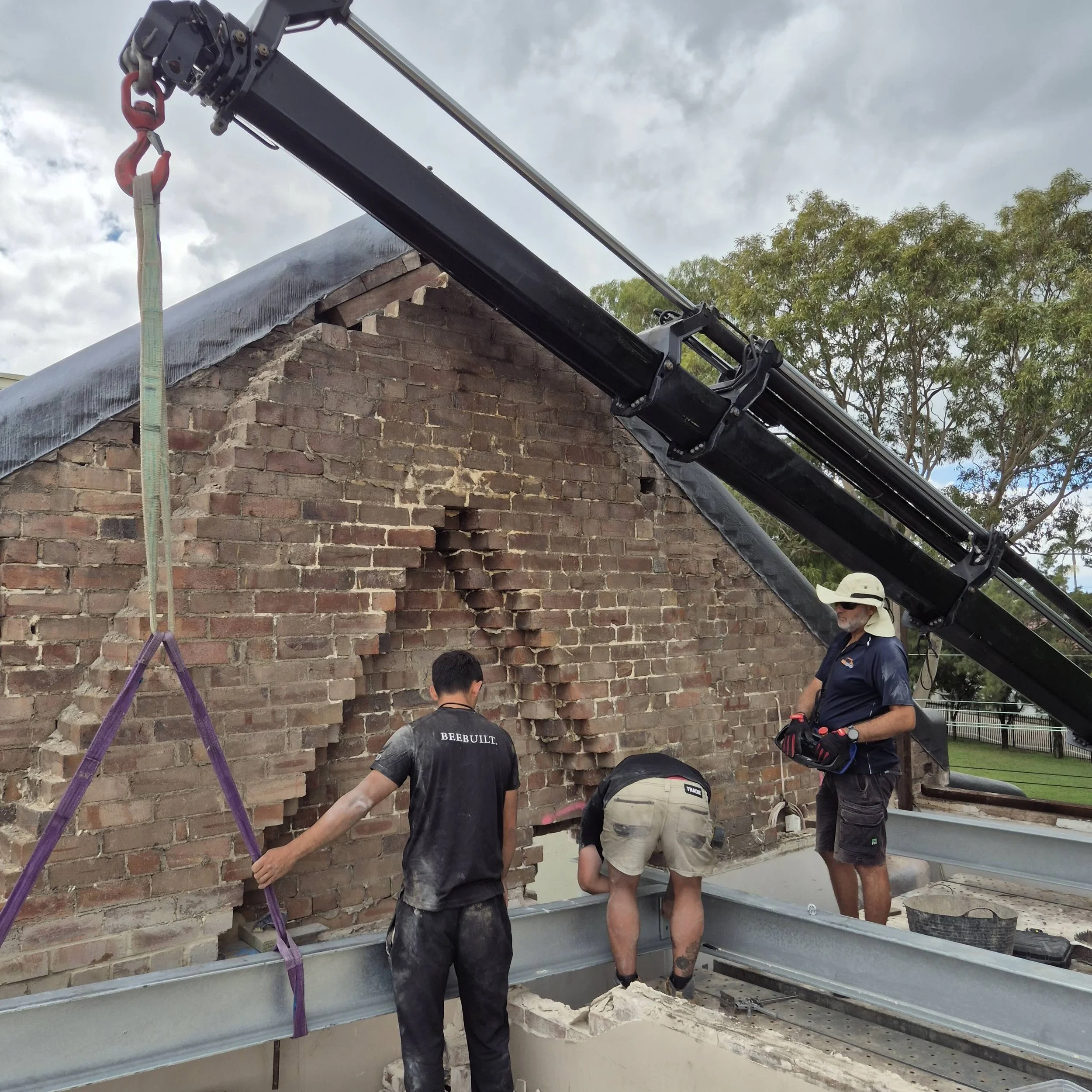 Construction workers inspecting a brick chimney during building or renovation process, with a crane lifting materials nearby.