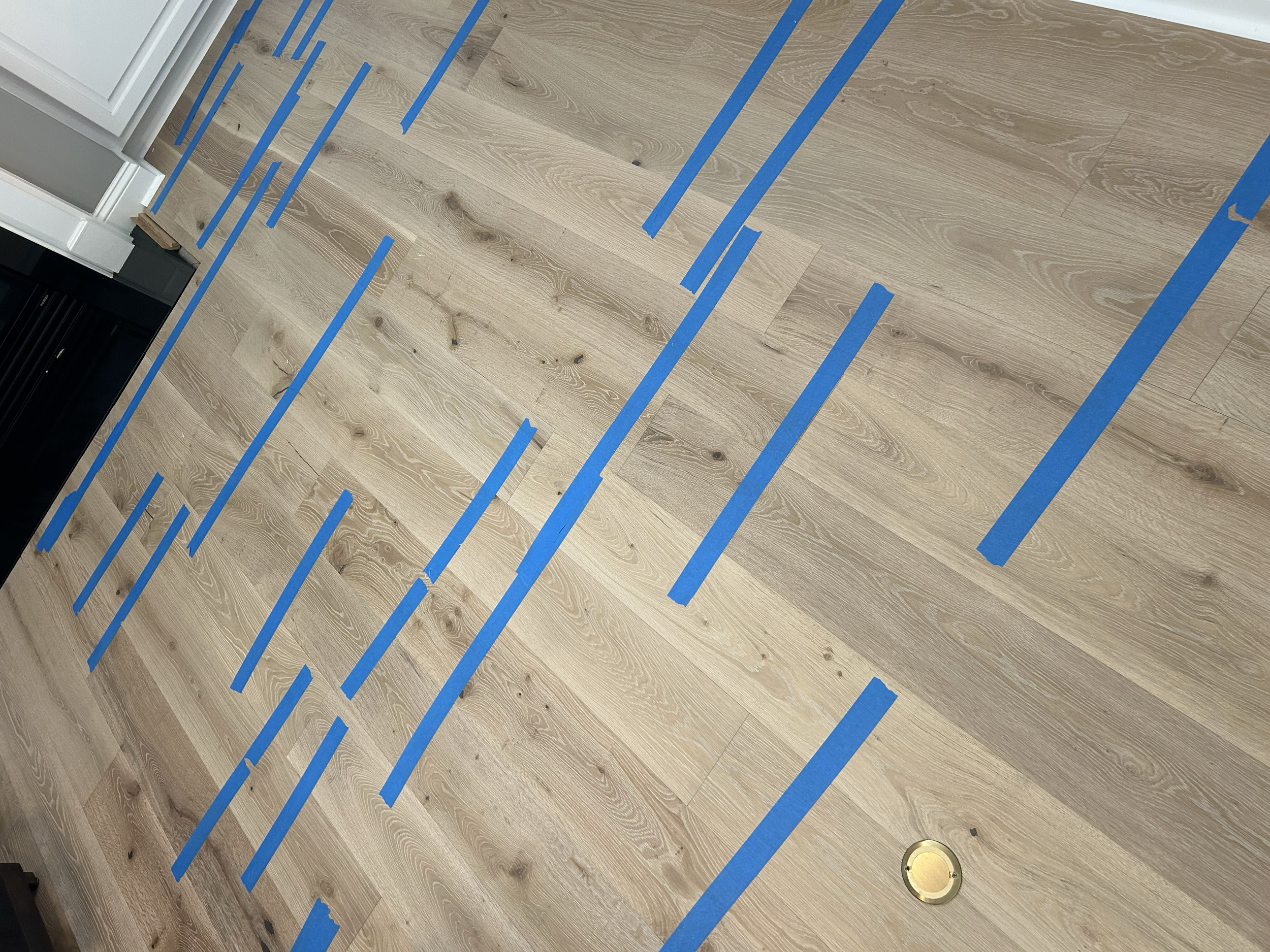 Wooden floor with blue painter's tape creating lines and markings.