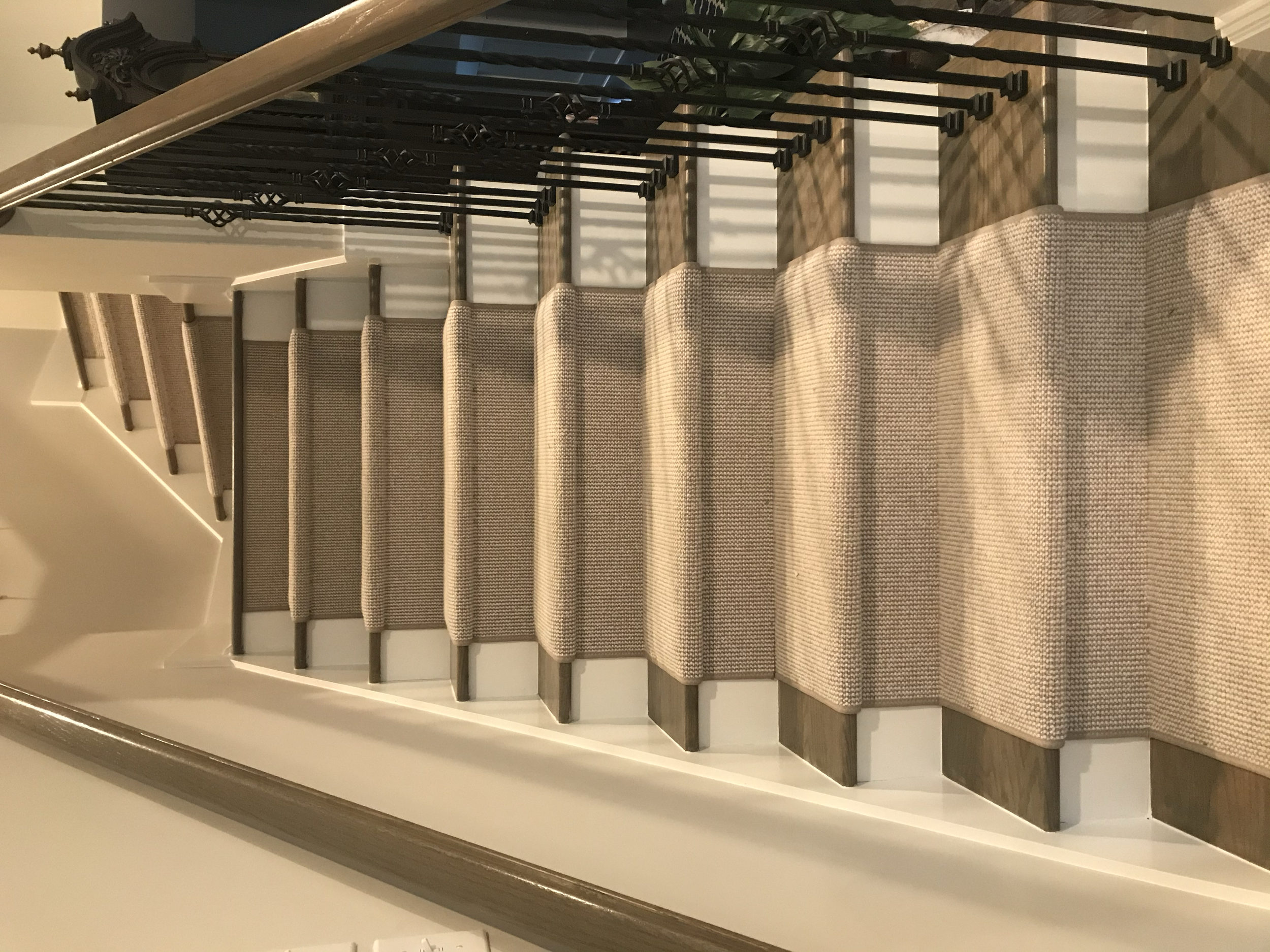 Inside view of a staircase with carpeted steps, wooden trim, and decorative black metal railing.