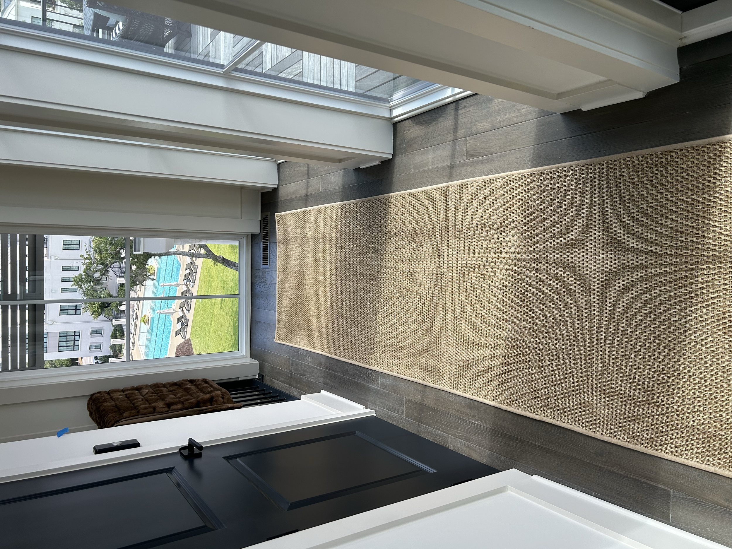 View from inside a home with a long beige rug on dark wood floors, a sliding glass door leading to a balcony, and a view of a swimming pool and apartment buildings outside