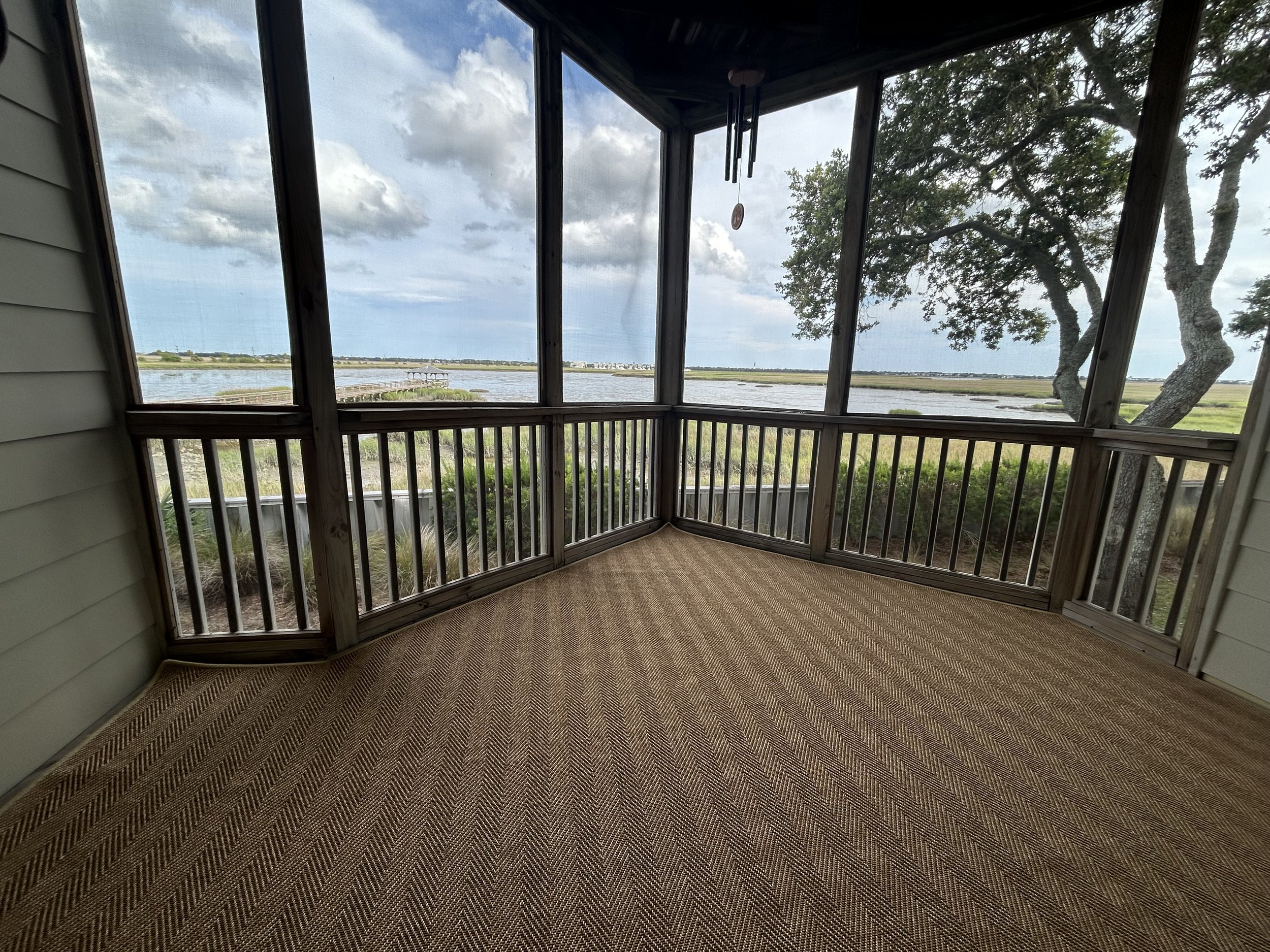 View from a screened porch overlooking a marshland with water, trees, and cloudy sky in the distance.