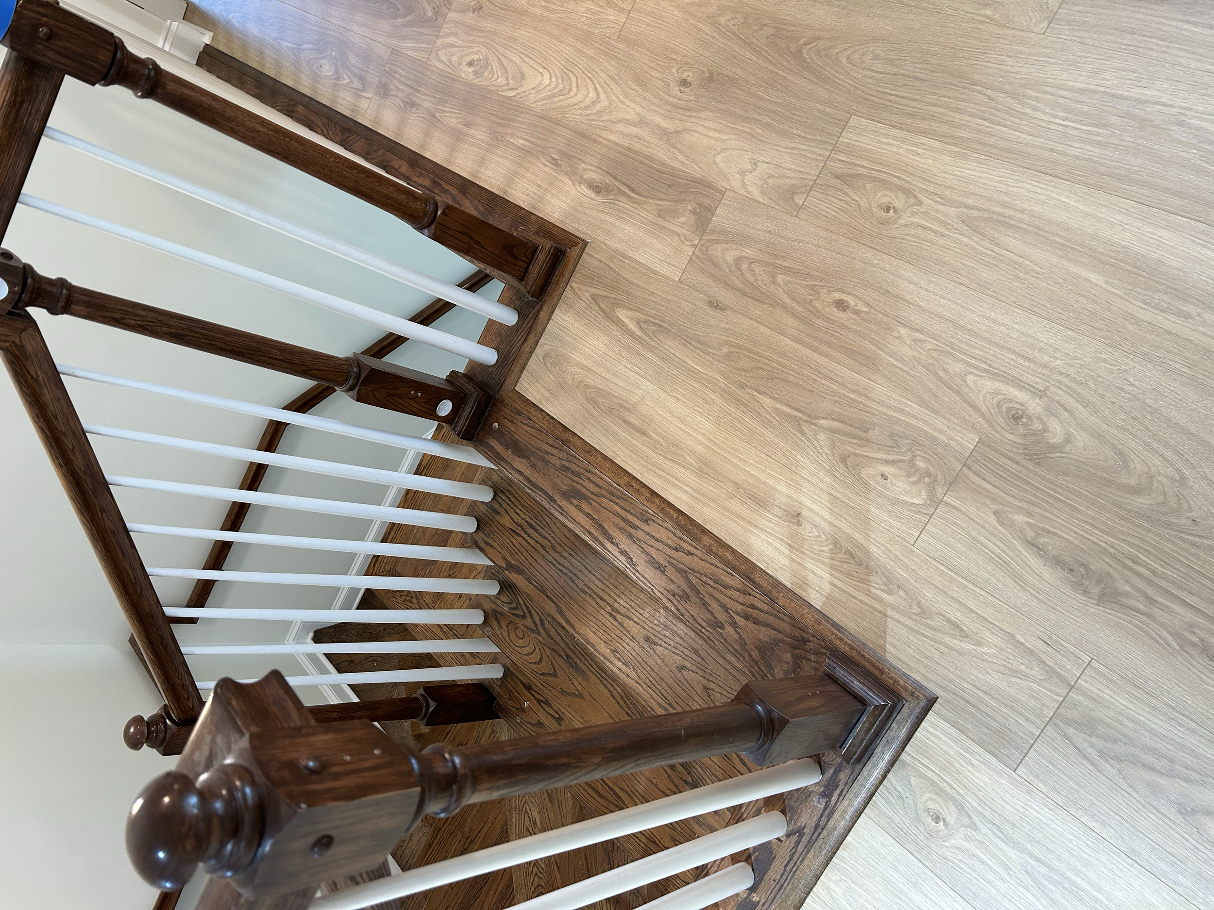 View of a staircase with wooden posts and white spindles, brown and light wood flooring.