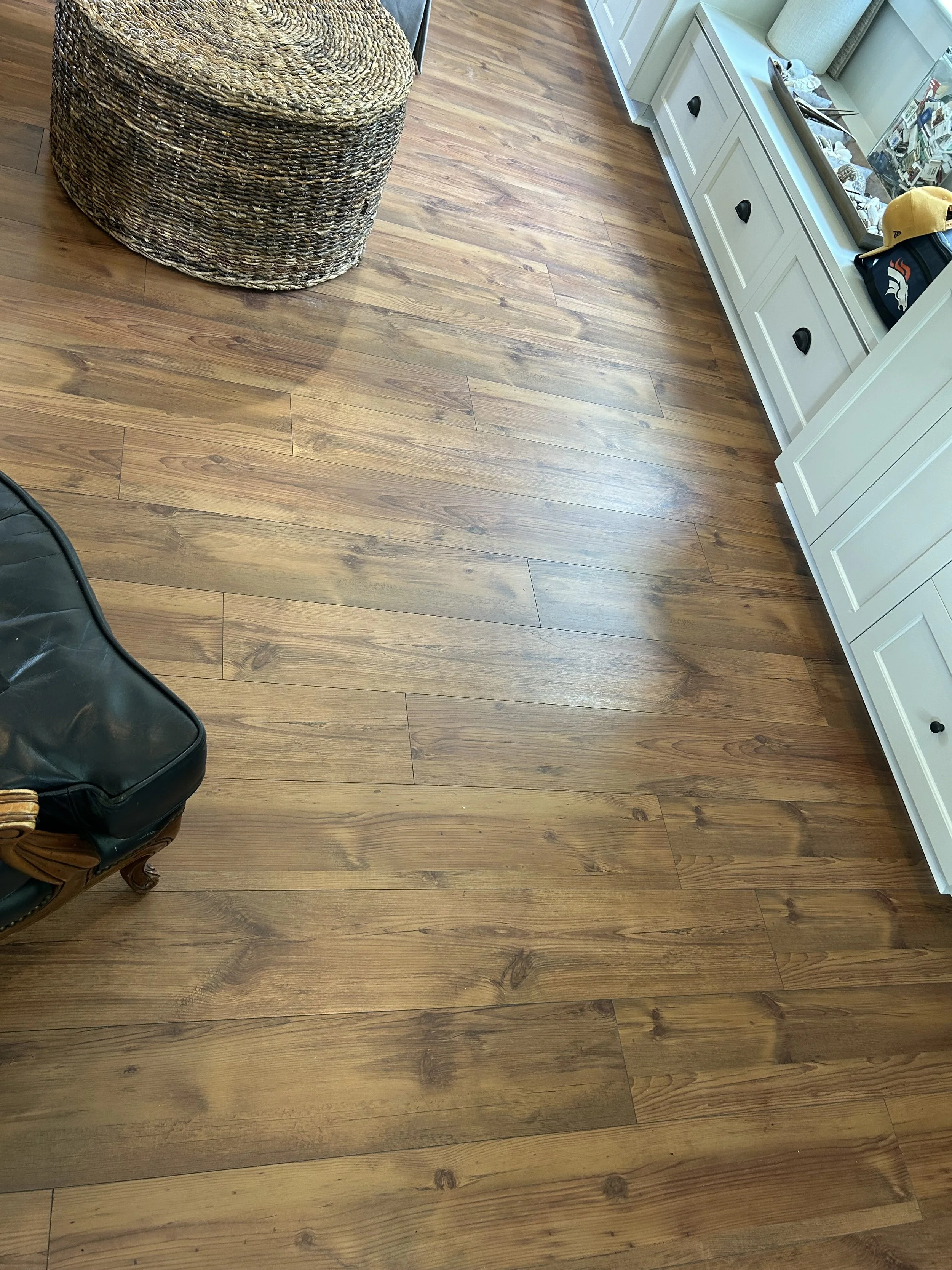 A wooden floor with a wicker basket, a white cabinet with black handles, a mirror, some sunglasses, a cap, and several magazines and papers.