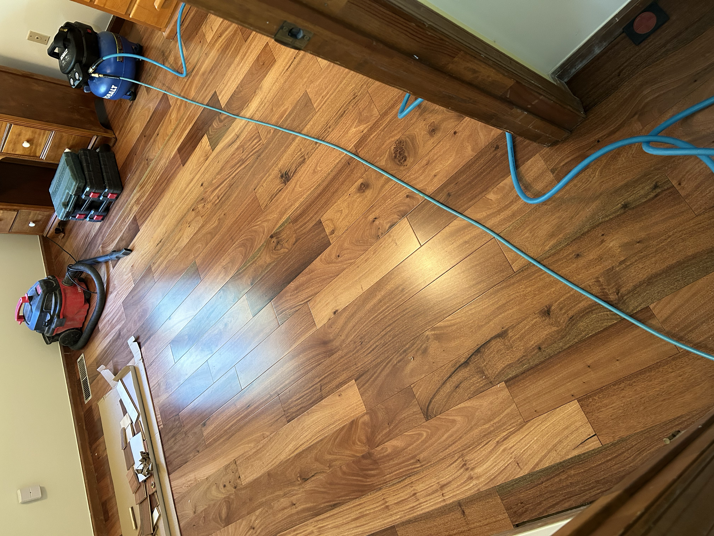 Room with hardwood floor being cleaned using a vacuum and carpet cleaner, with tools and equipment stored nearby.