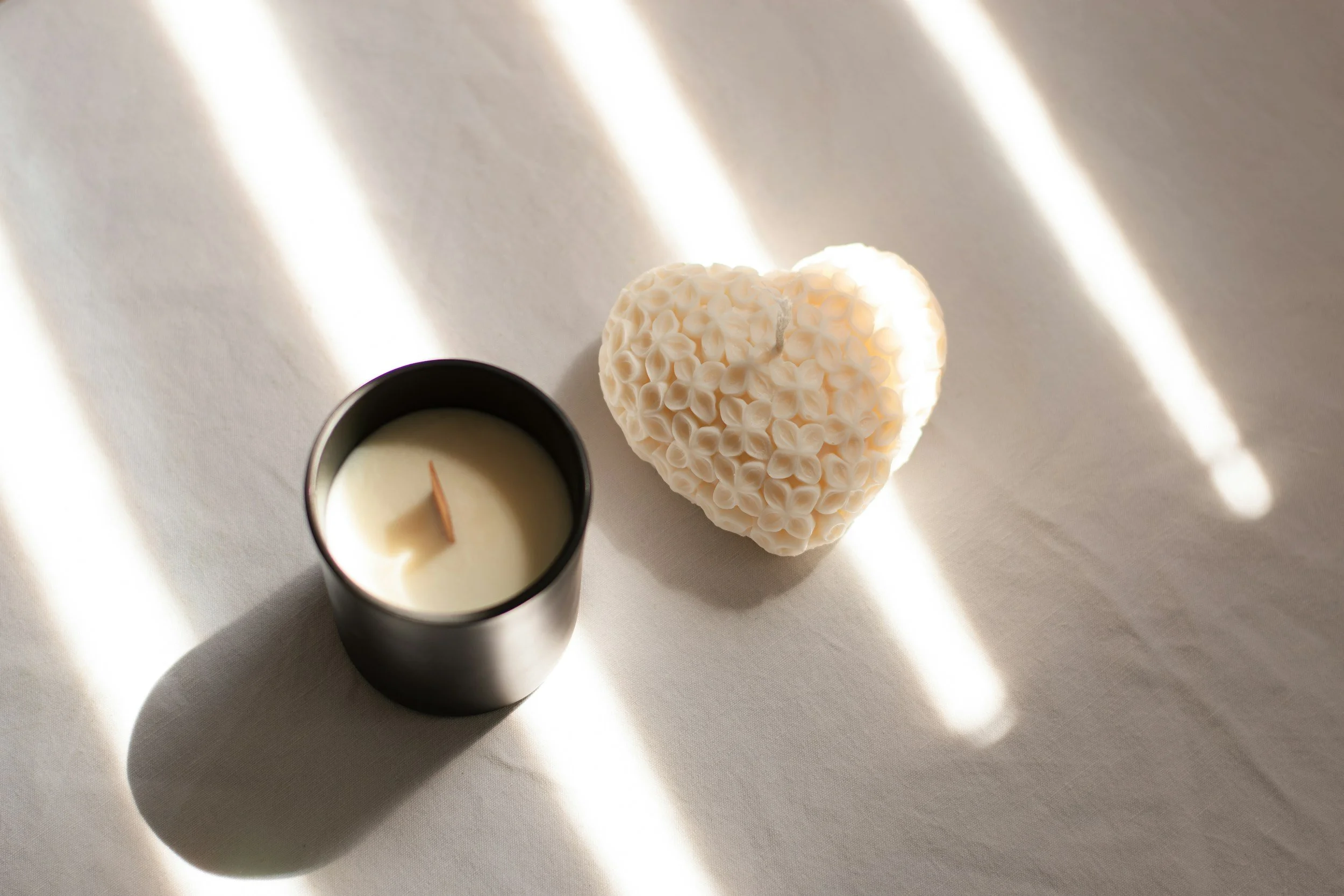 Candle and heart-shaped sculpture illuminated by soft natural light.