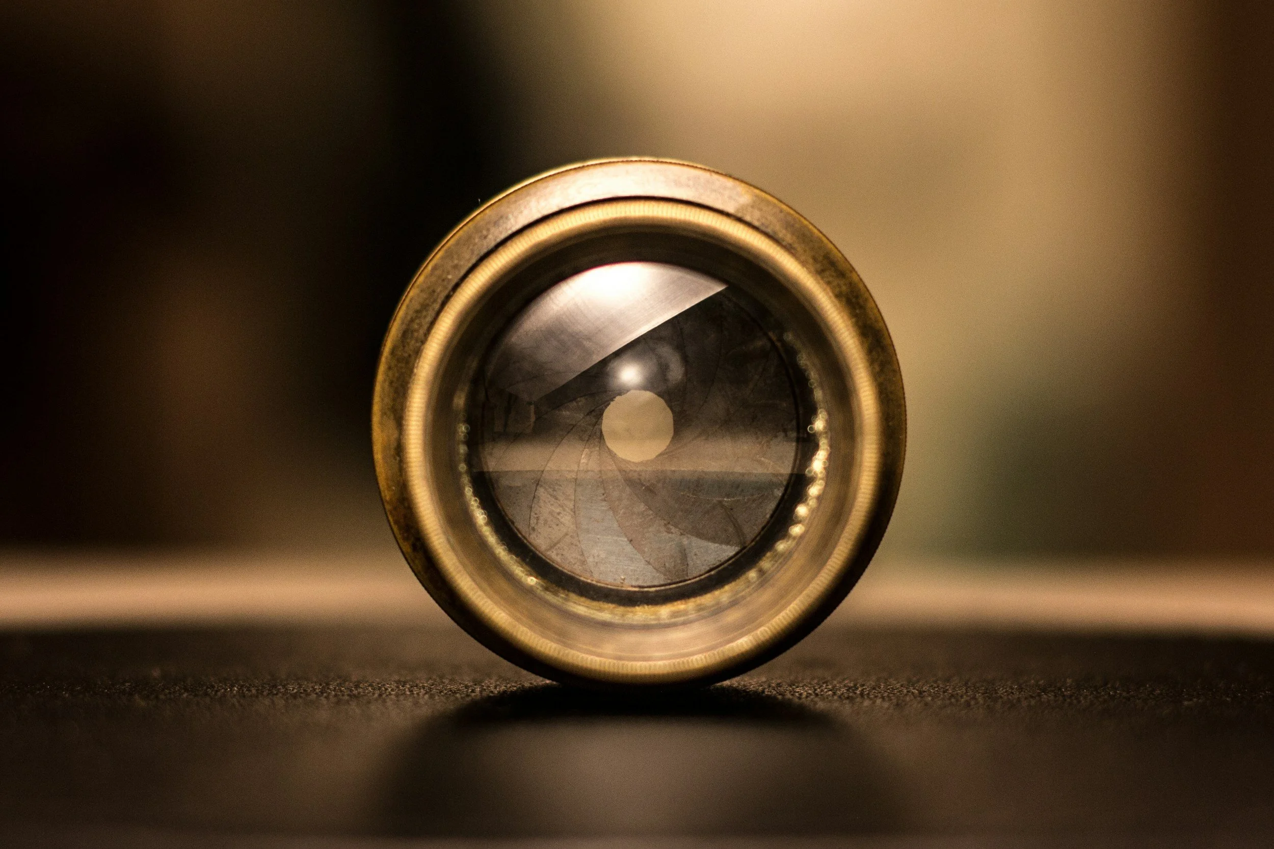 Close-up of a camera lens from the front, showing the glass elements and metallic ring, with a blurred background.