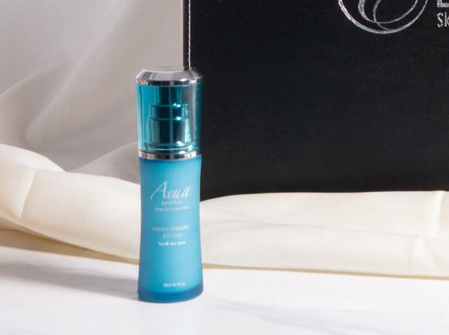 Aqua Mineral Uplift Firming Eye Gel in a blue pump bottle with a silver cap, displayed on white fabric beside a black product box.