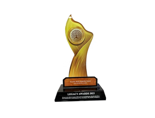 A golden award trophy shaped like a stylized human figure with a circular top, mounted on a black base with a plaque that reads 'Elite Skin Perfection, Legacy Awards 2023'.