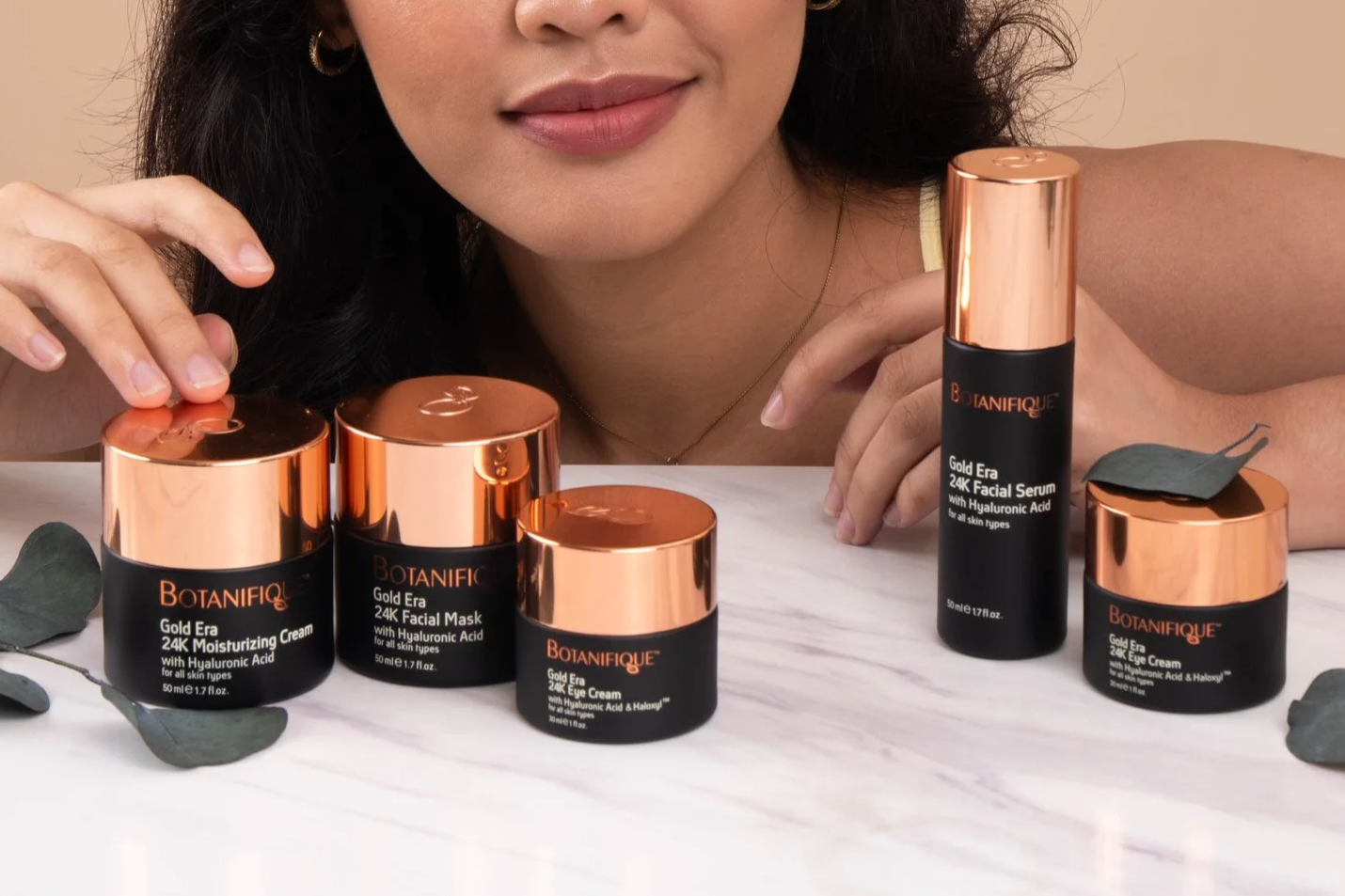 Botanifique Gold Era skincare collection featuring 24K moisturizing cream, facial mask, eye cream, and facial serum displayed with a model.