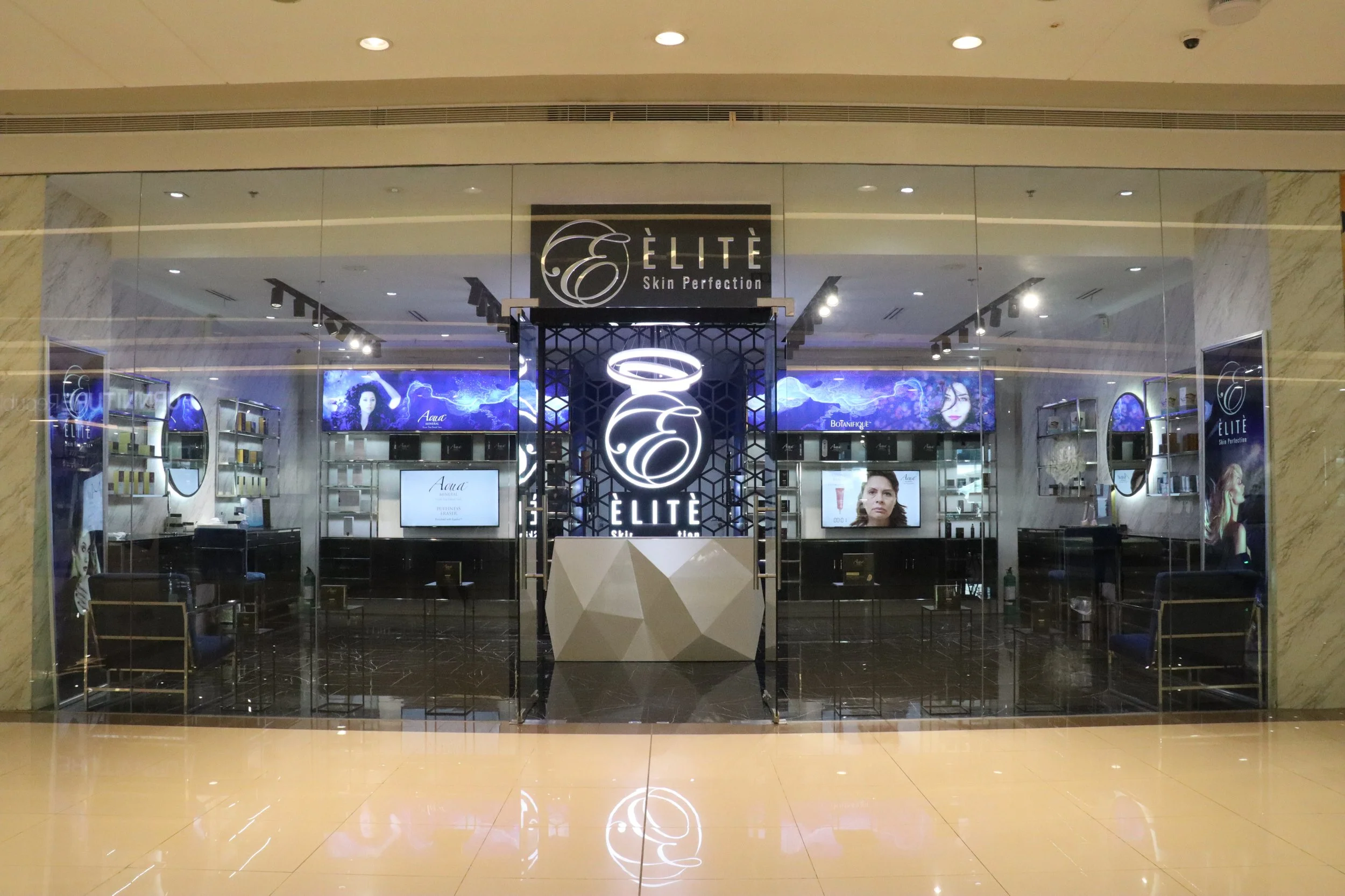 Storefront for ELITE Skin Perfection with illuminated logo and digital advertisements inside shopping mall.