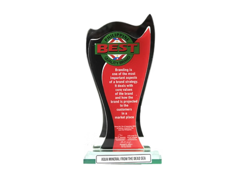 Trophy or award with a black base and a curved, black and red top. The top features a green, red, and black logo with the word "BEST" and text indicating it is from the Philippines, along with a paragraph about branding. The base has a white plaque with the text "AQUA MINERAL FROM THE DEAD SEA."
