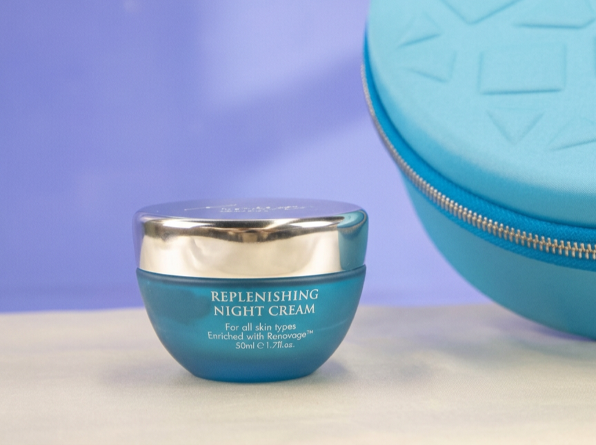 Close-up of the Aqua Mineral Replenishing Night Cream in a blue jar with a silver lid, displayed on a light surface with a blue travel case in the background.