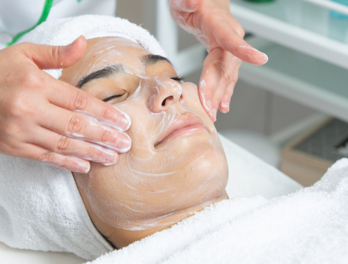 Woman receiving a facial treatment with soap or cleanser applied by esthetician in a spa setting.