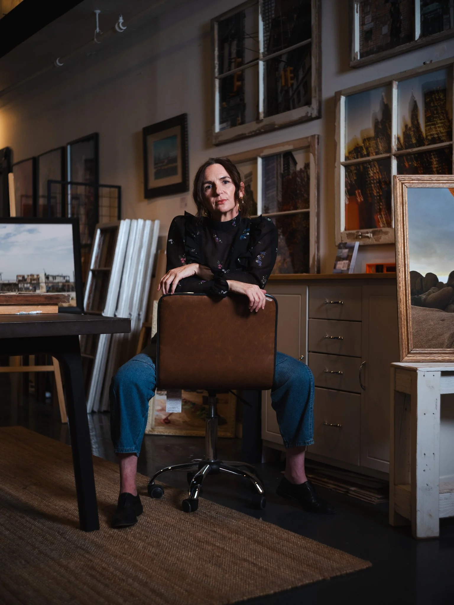 Woman sitting on a chair in an art gallery surrounded by framed paintings and photographs on the wall.
