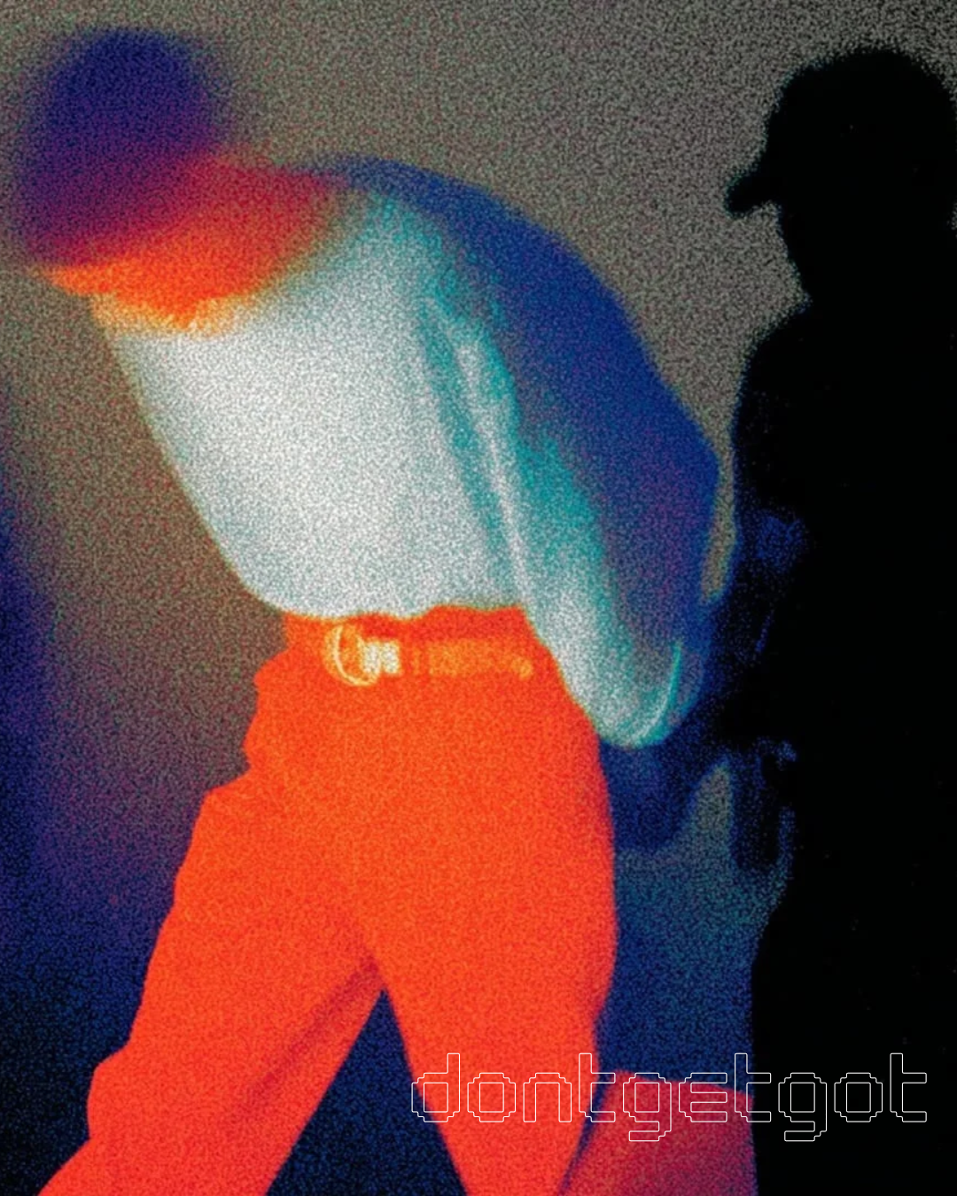 Silhouette of a person wearing a hat, standing next to a large, colorful abstract sculpture with neon colors and a textured surface.