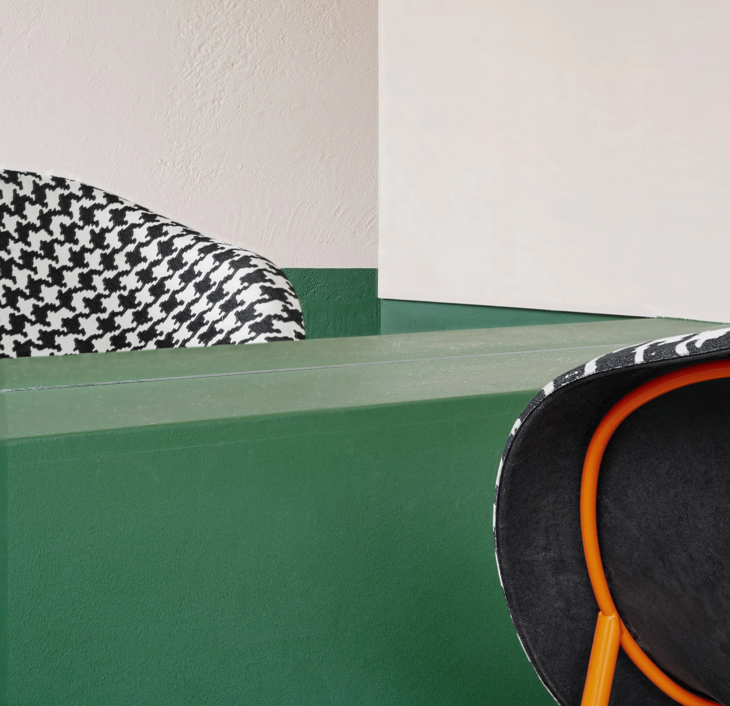 Close-up of a black and white houndstooth patterned object on a green surface with an orange cable and a black surface in the background, and a white textured wall in the background.