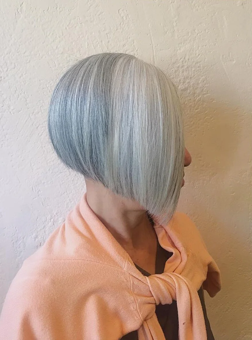 Side view of a woman with a sleek, layered, silver-gray bob haircut wearing a light pink hoodie.