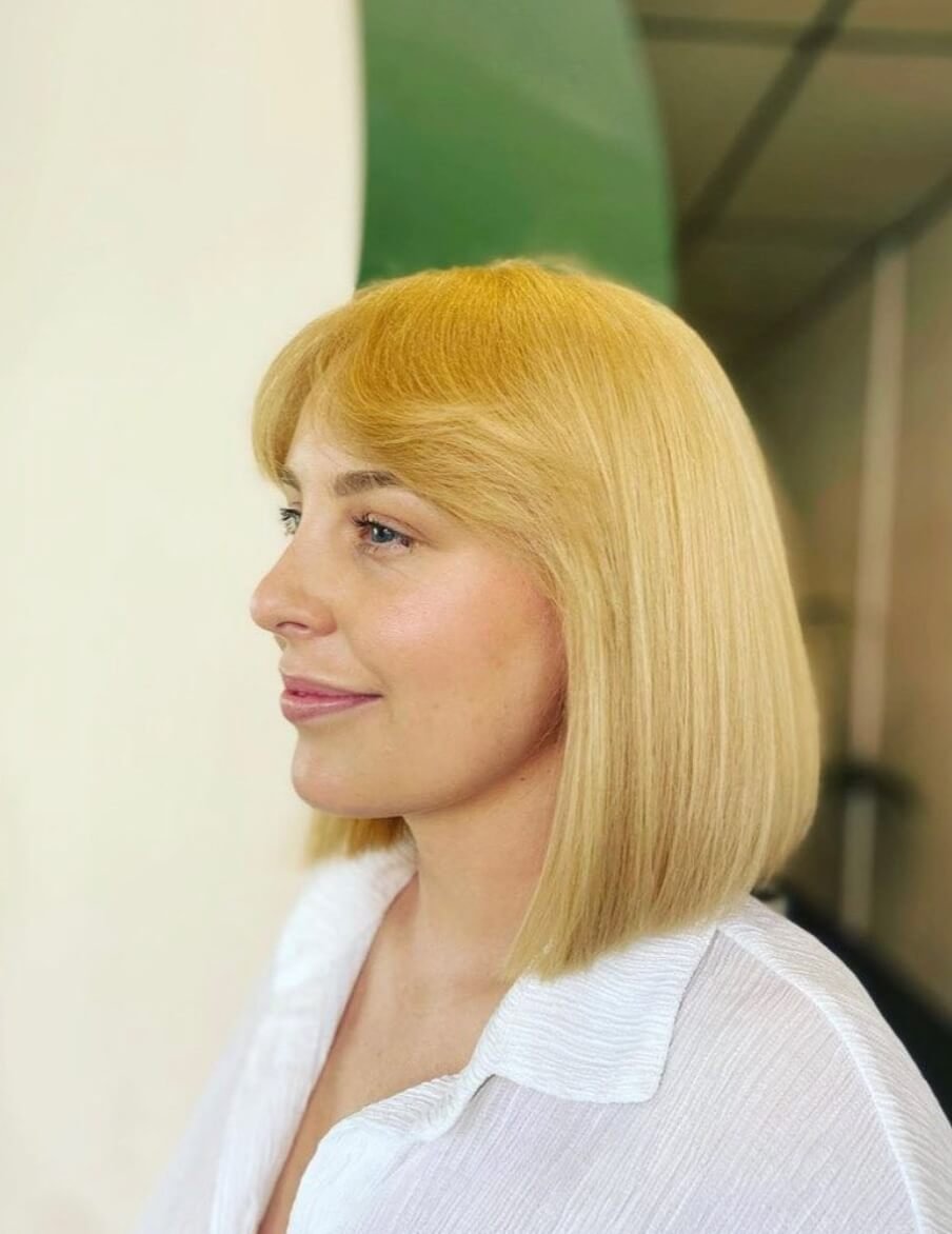Profile view of a woman with shoulder-length blonde hair wearing a white shirt.