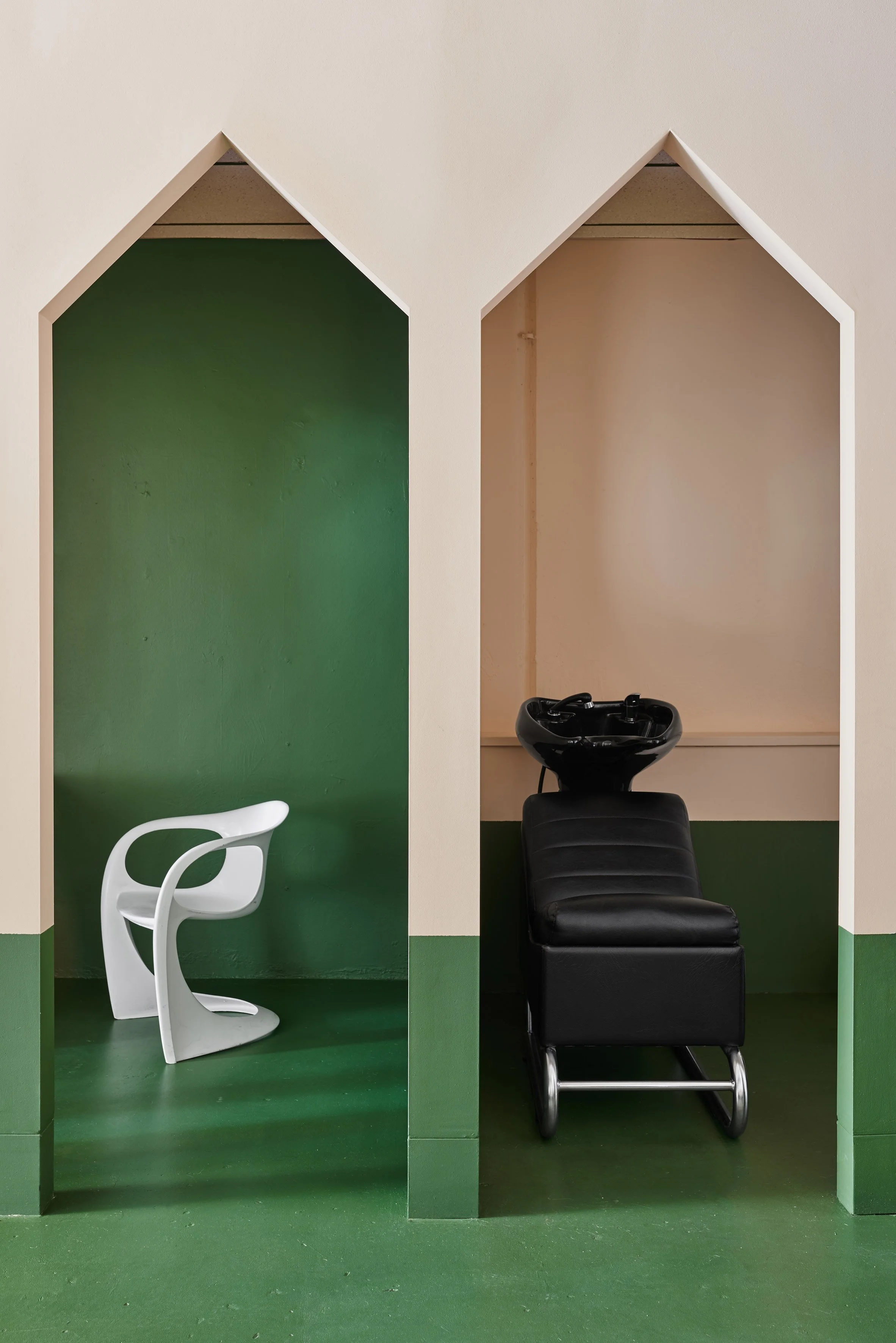 Interior of a salon or barbershop with two stylist stations. The left station has a white modern chair, and the right station has a black styling chair with a sink for washing hair.