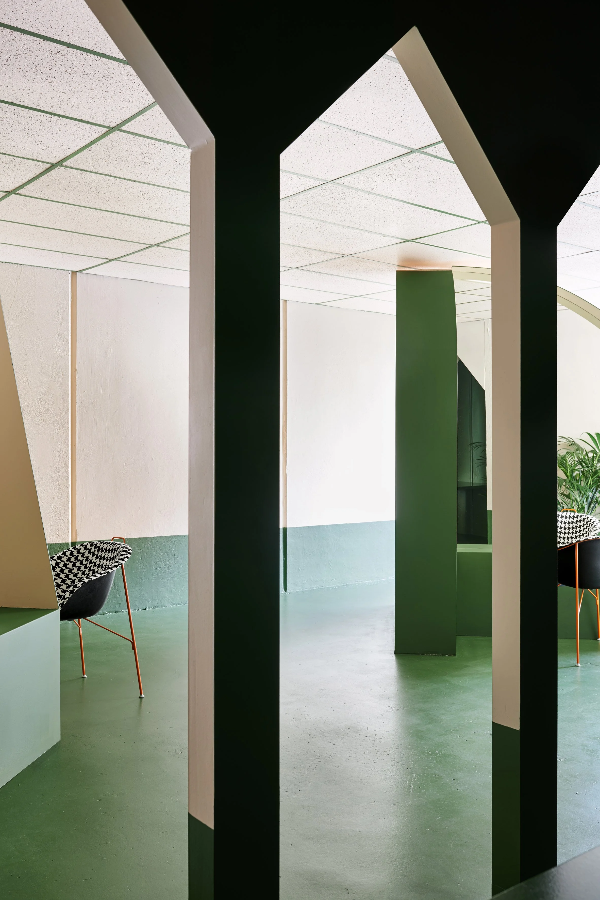 Modern interior with green flooring, white walls, black and white patterned chairs, and architectural black and white columns.