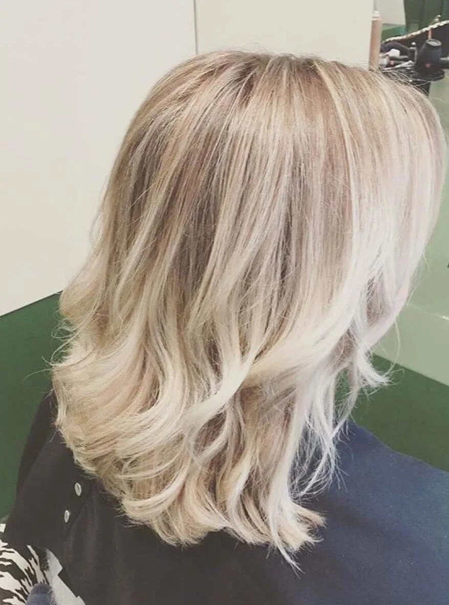 Blonde wavy shoulder-length hair viewed from the back, sitting in a salon chair.