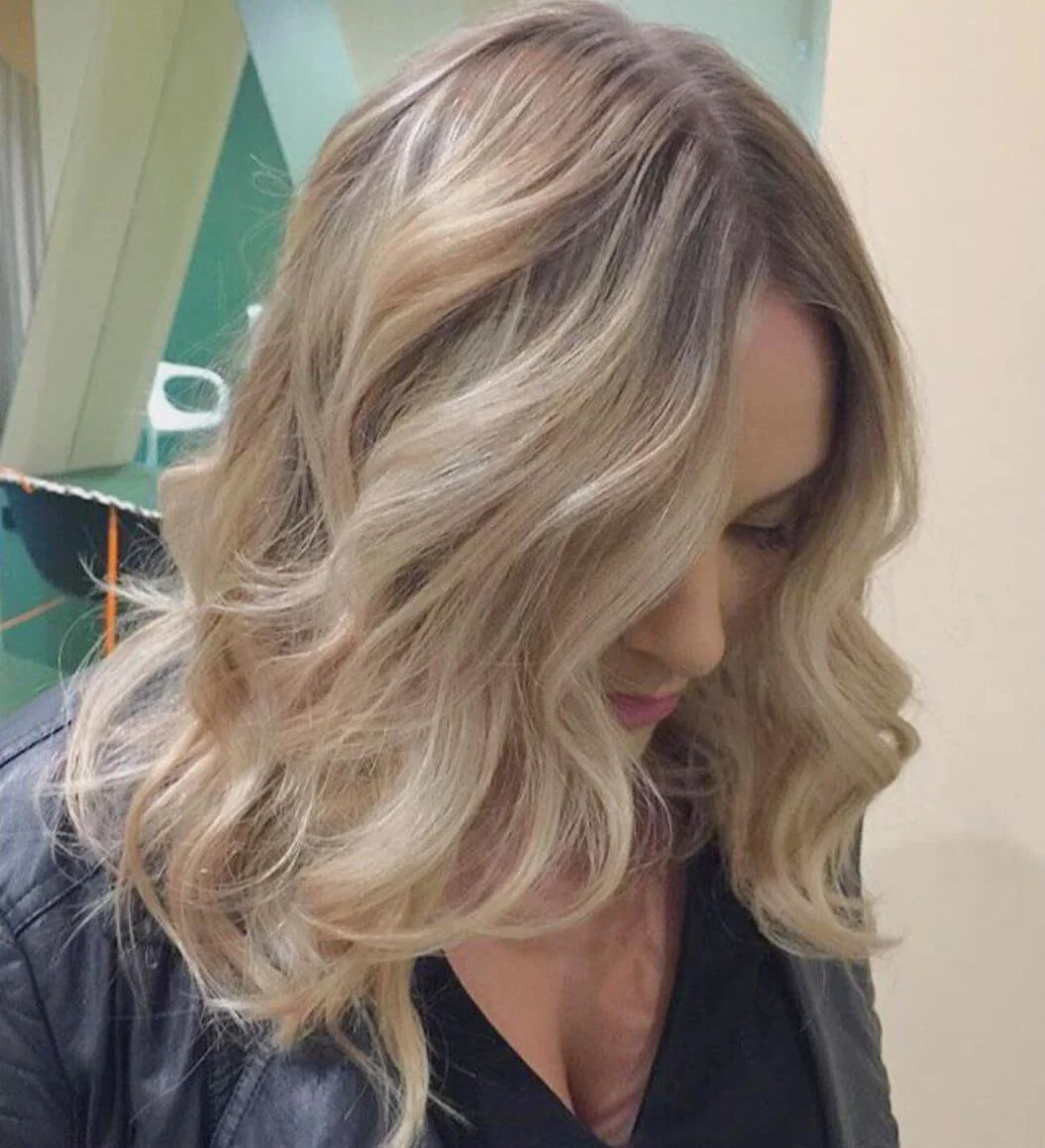 Close-up of a woman with wavy, blonde hair looking down.