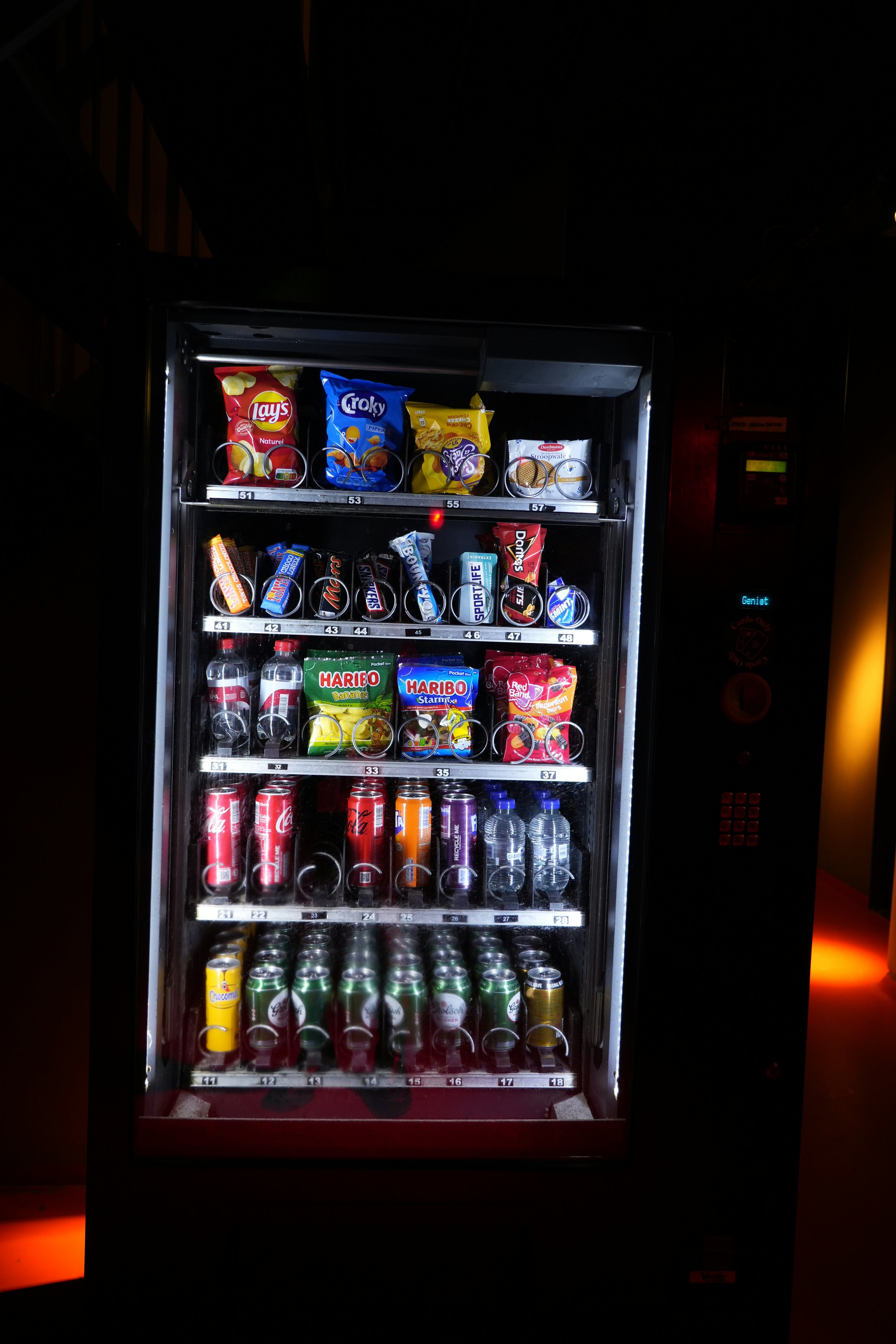 A vending machine filled with snacks and beverages in a dark room.