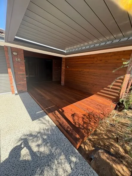 Modern house garage with a wooden ramp leading inside, partial brick and wood exterior, potted plant on the side, and a gravel driveway.
