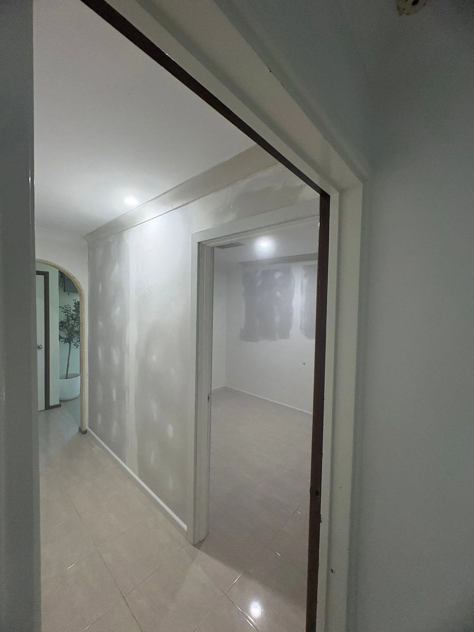 Interior view of a house hallway with a glass sliding door, tiled floor, white walls, and a doorway leading to another room.
