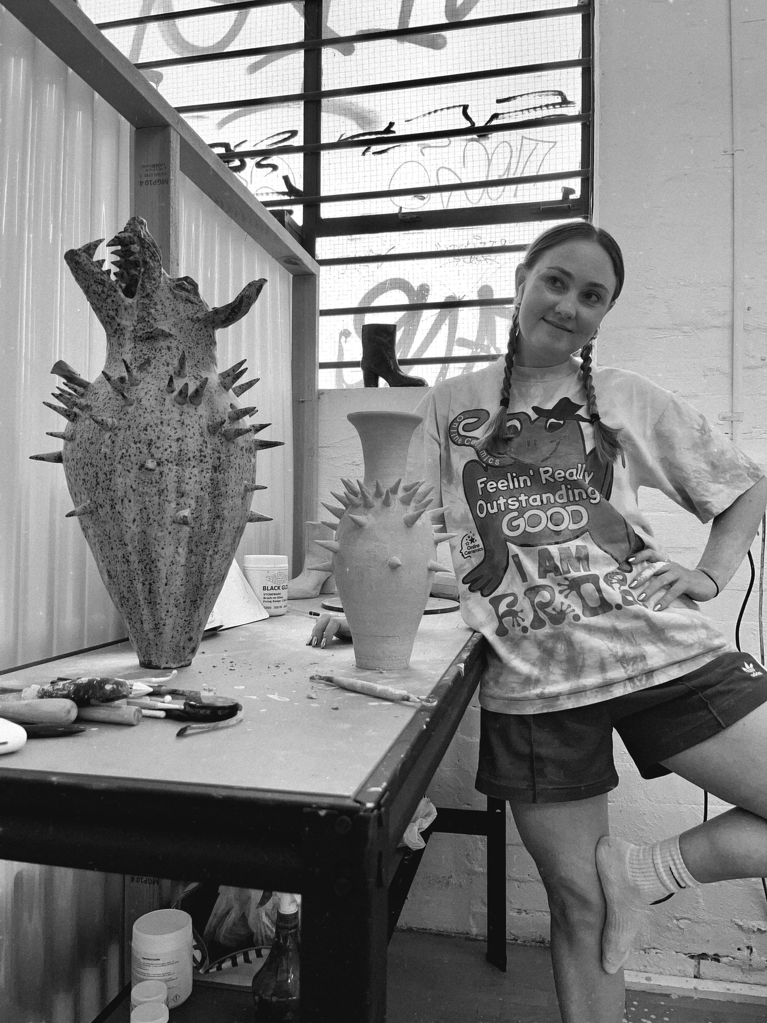 A woman in a pottery studio standing by a work bench with a large ceramic vase with spikes and a wolf head.