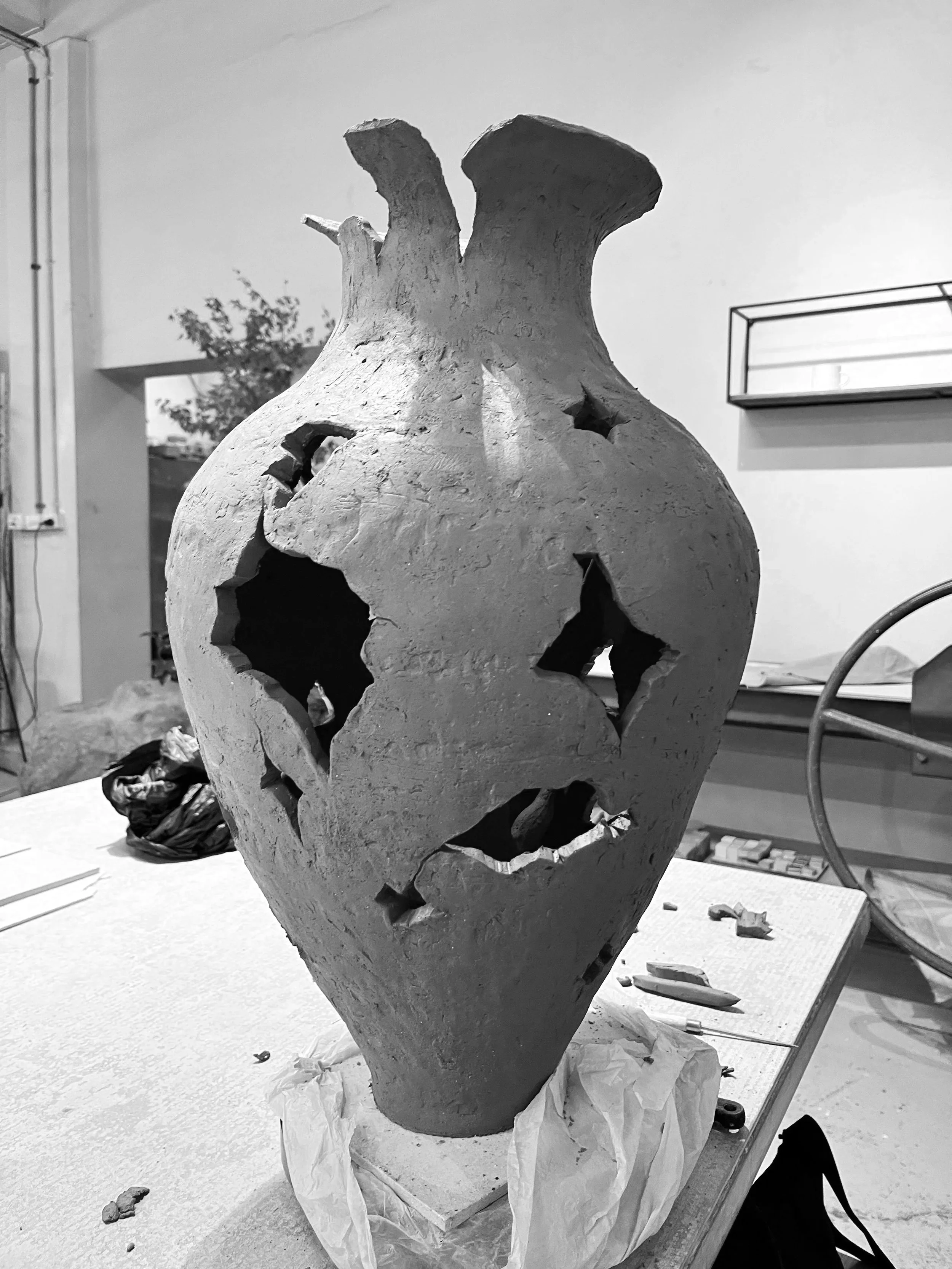 A ceramic vase still in the process of being made, with holes, placed on a worktable in a pottery studio.
