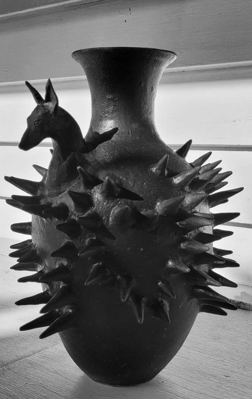 Black and white photo of a ceramic vase decorated with a doberman dog and covered in spikes.