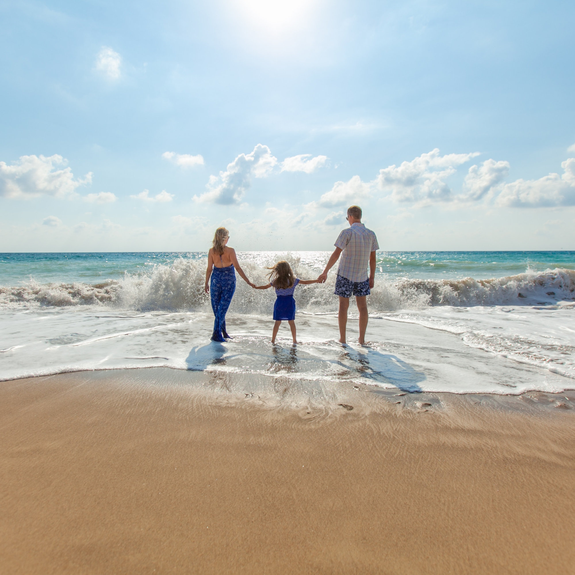 Familia caminando por la playa durante el día, con el mar y el cielo con nubes blancas en el fondo.