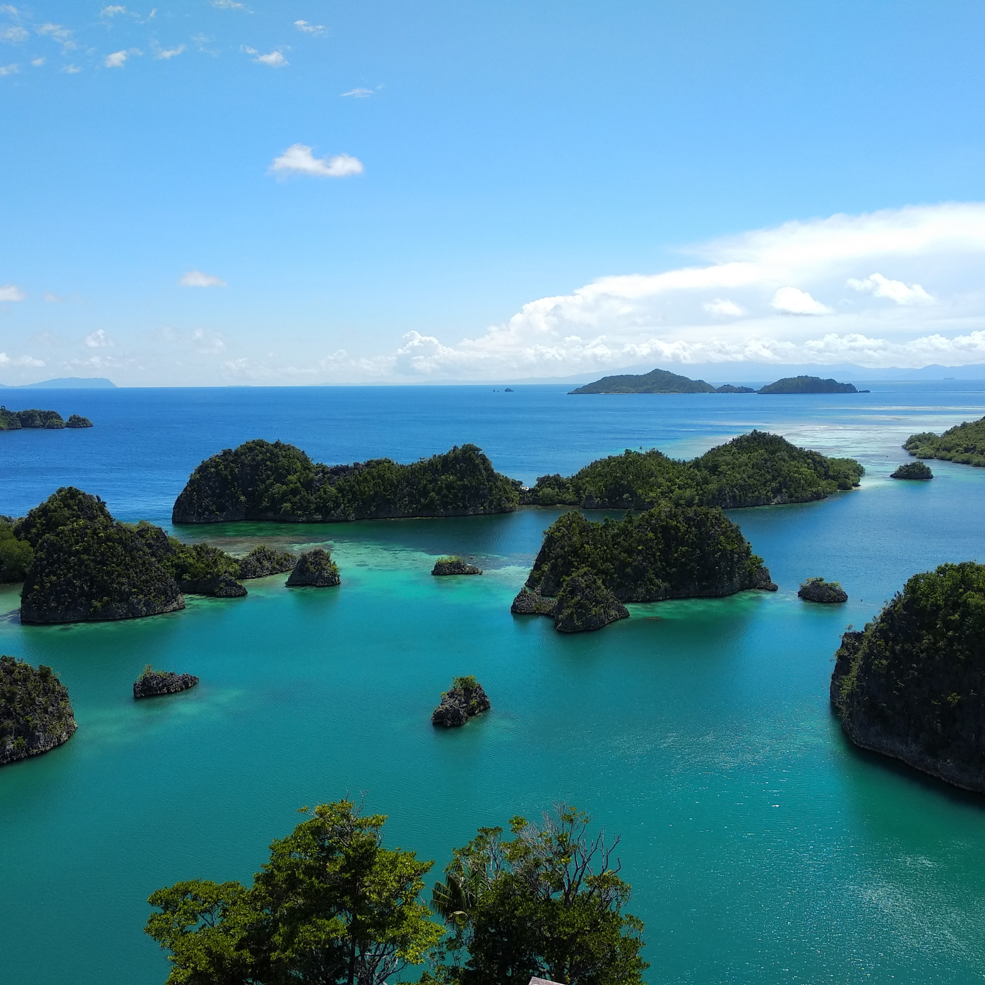 Vista de un mar azul con varias islas cubiertas de vegetación, algunas en el primer plano y otras en el fondo, bajo un cielo despejado con algunas nubes.