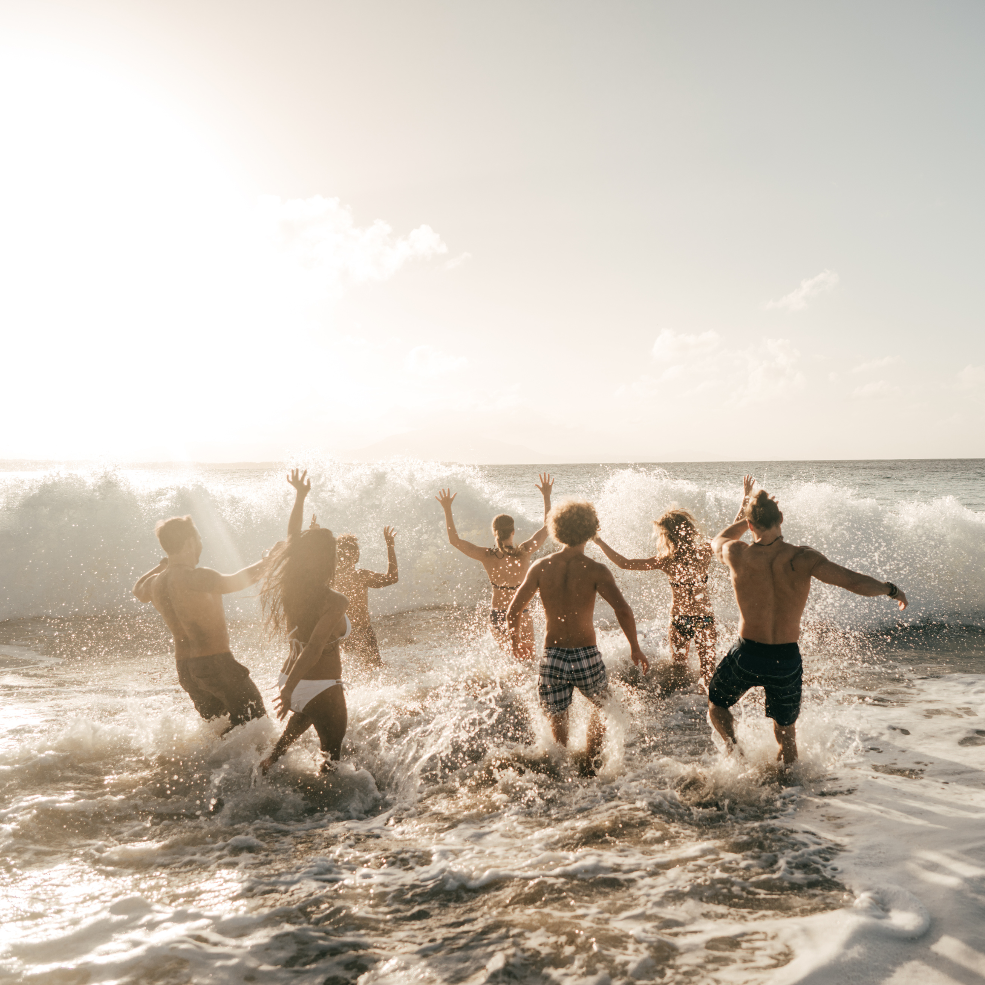Grupo de personas jóvenes disfrutando y corriendo en la orilla del mar con las manos al aire y el sol brillante en el cielo.